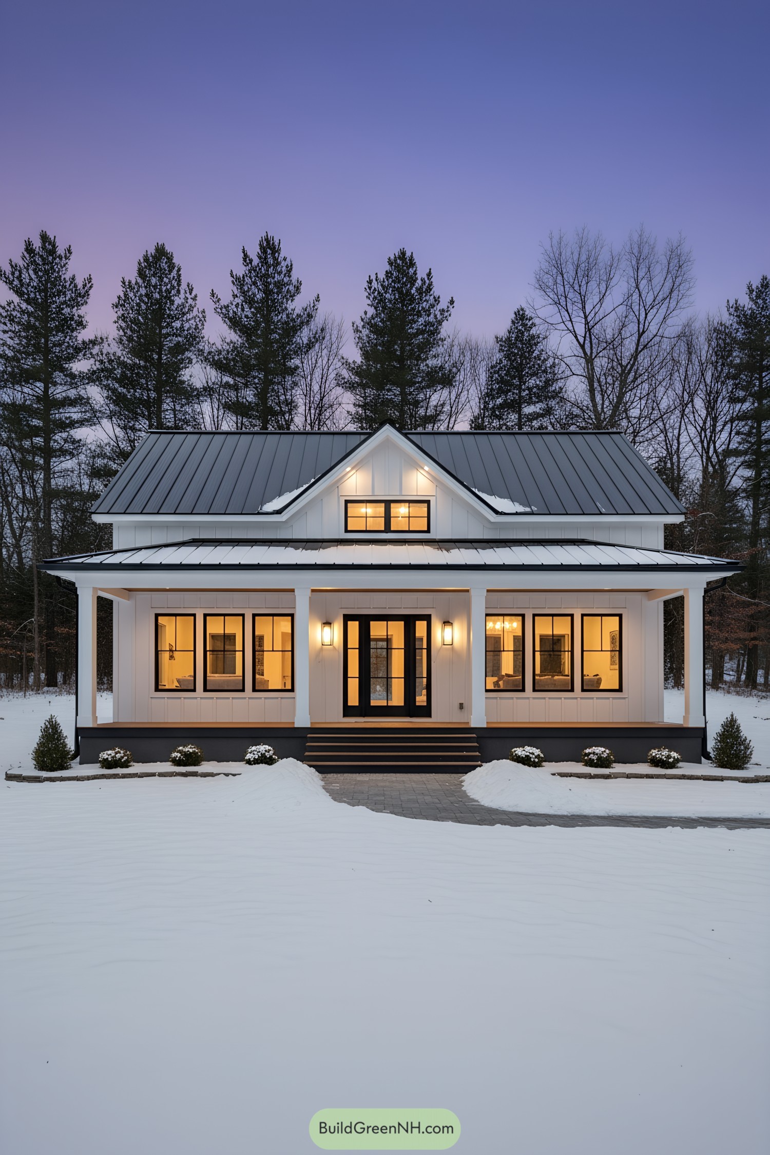 White modern farmhouse with black metal roof and warm-lit porch in snowy dusk