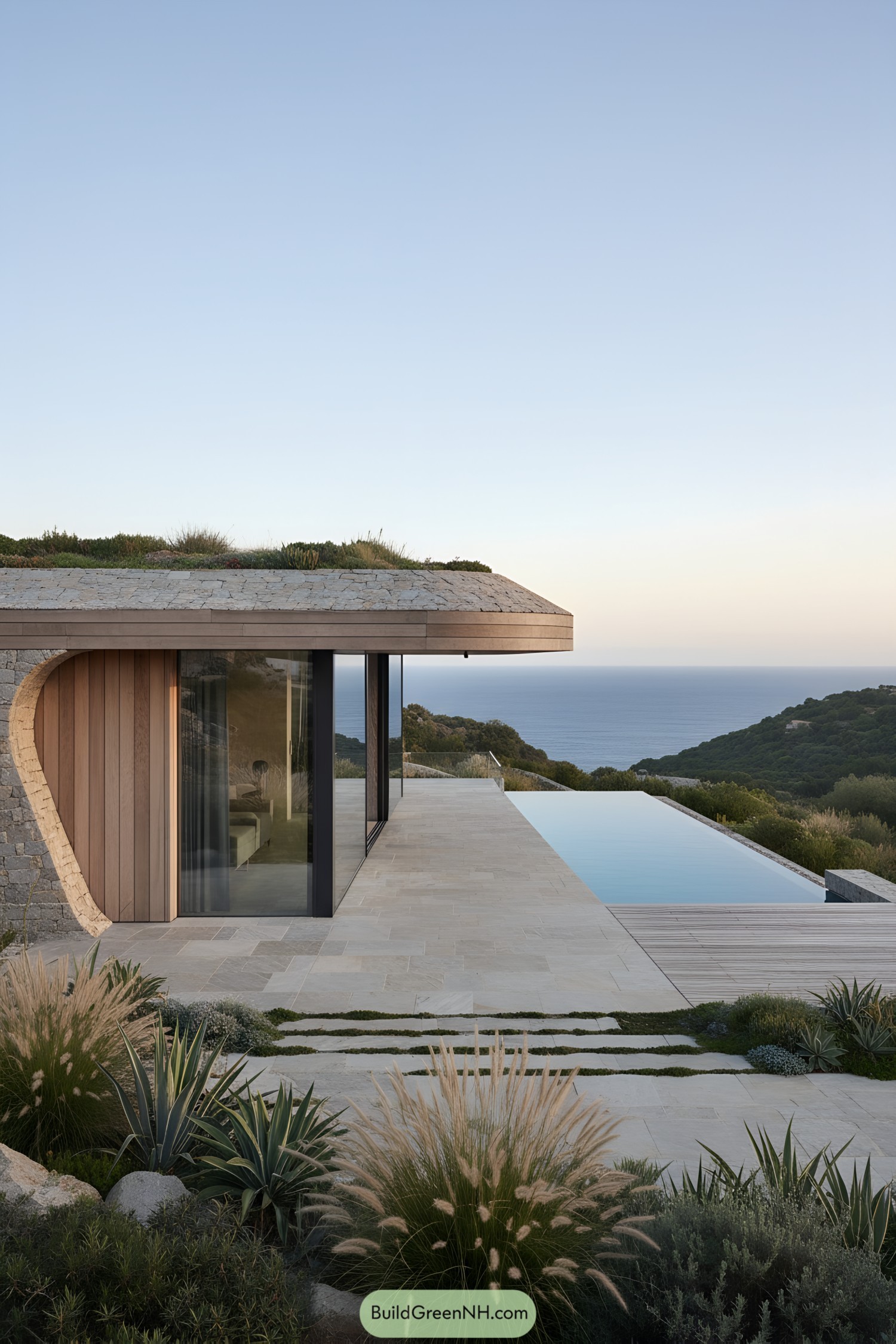 Low-slung modern house with a planted stone roof, glass walls, and an infinity pool facing the sea