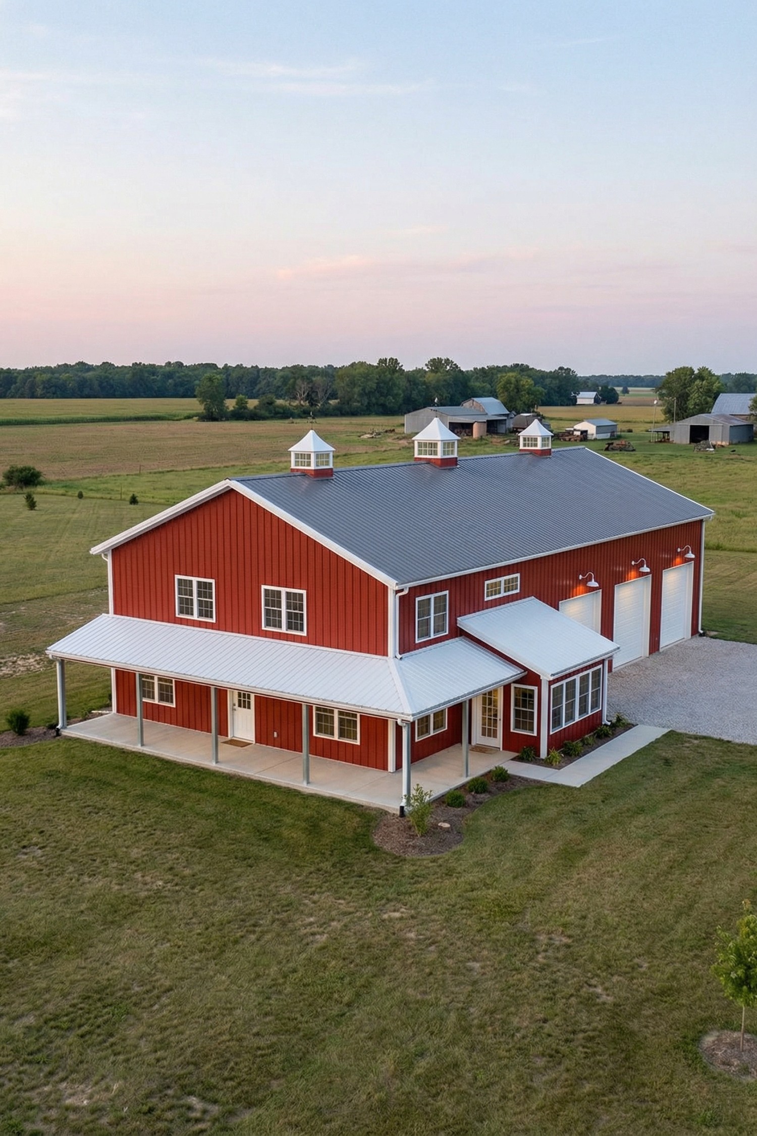 Red pole barn house with gray metal roof, white trim, wraparound porch, and triple garage bays