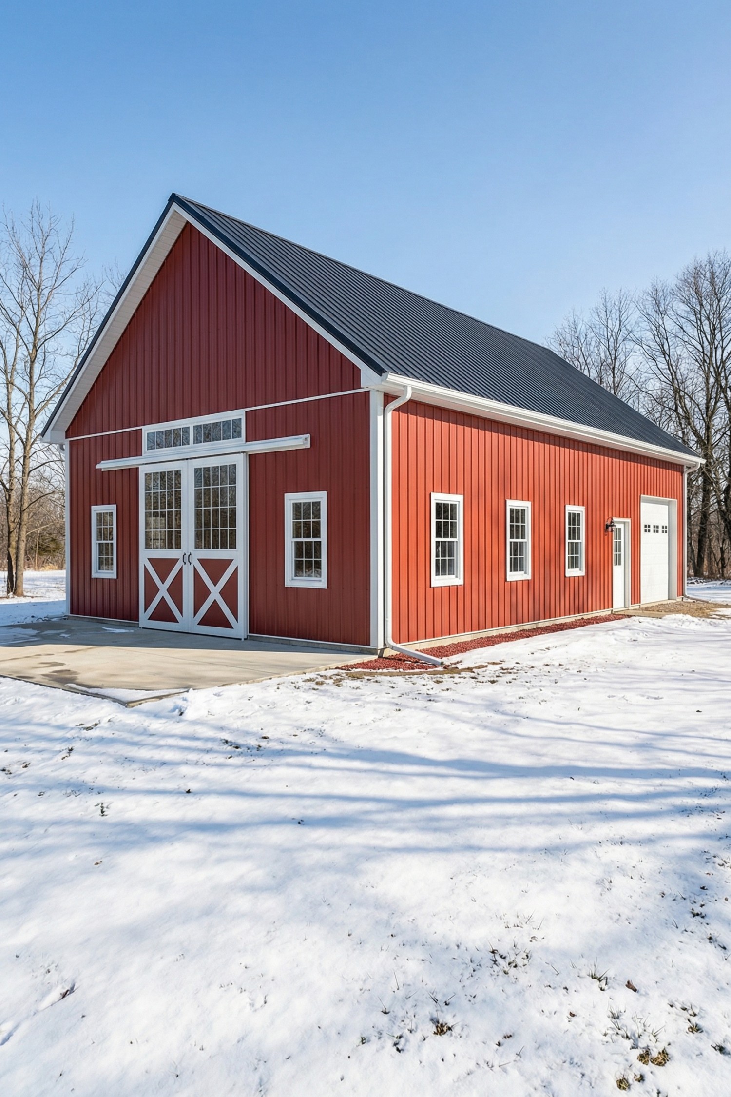Red gabled barn with black metal roof and white trim in a snowy landscape