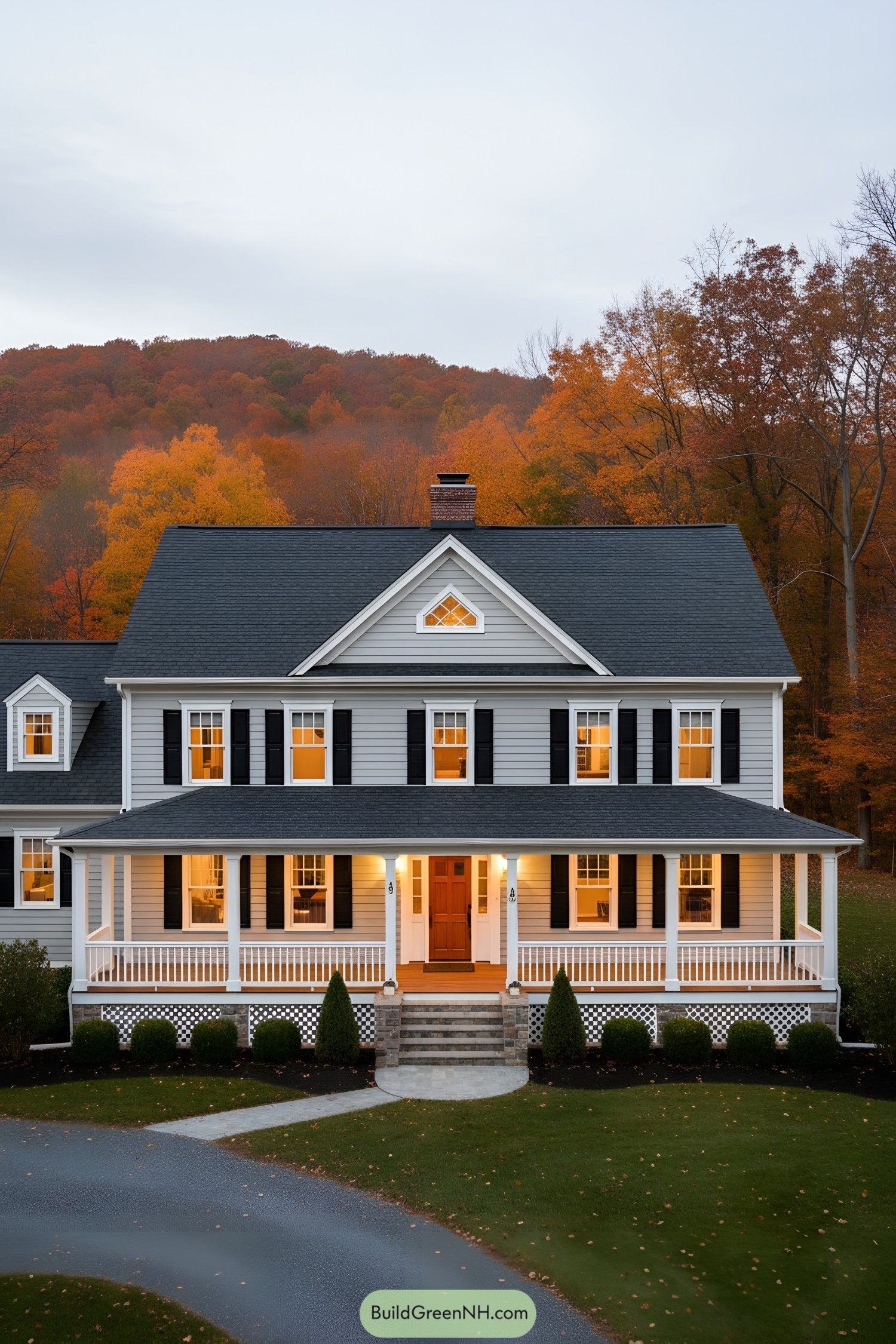 Two-story gray colonial with wraparound porch and black shutters at dusk
