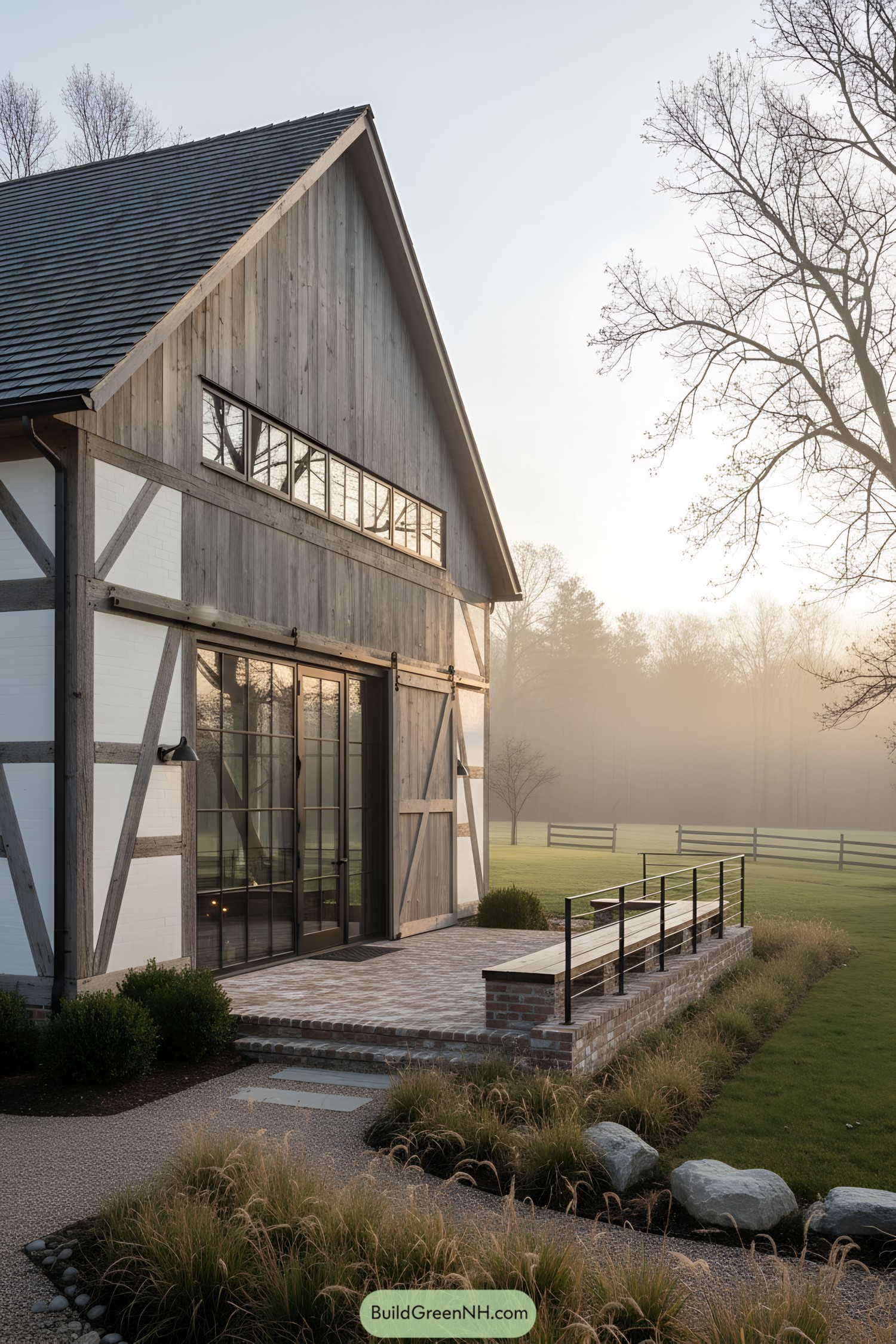 Converted barn with timber framing, tall steel-framed glass doors, and brick terrace at sunrise