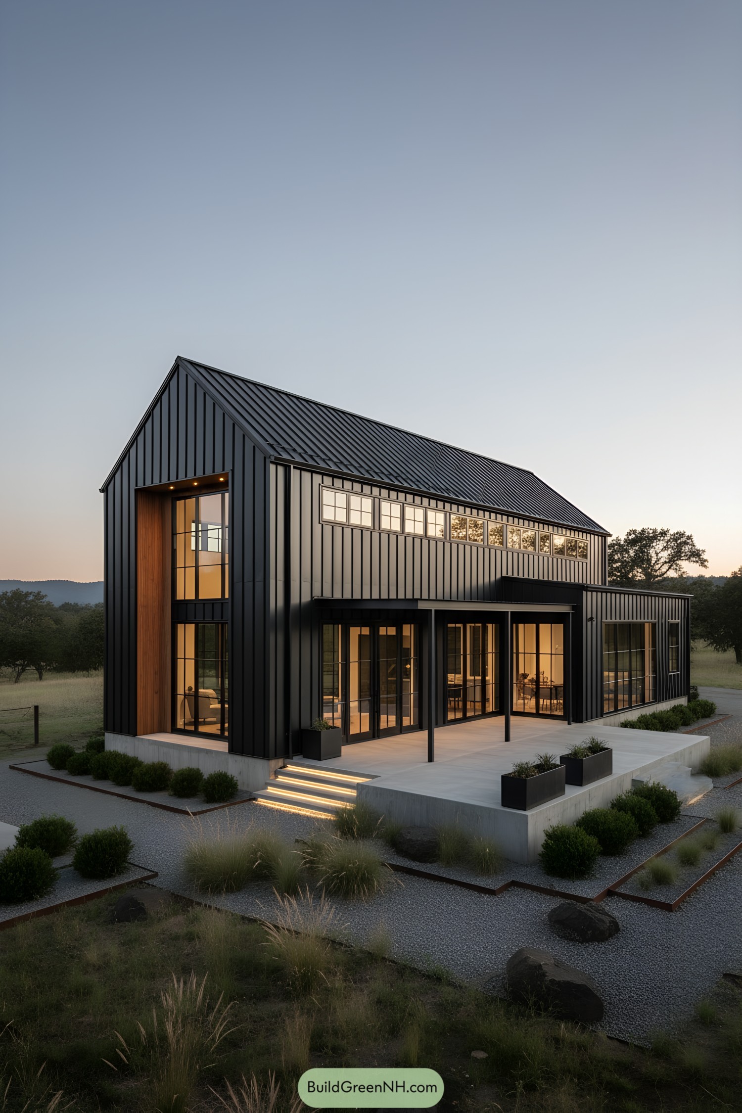 Black metal-clad modern barndo at dusk with warm interior lighting and sleek patio steps