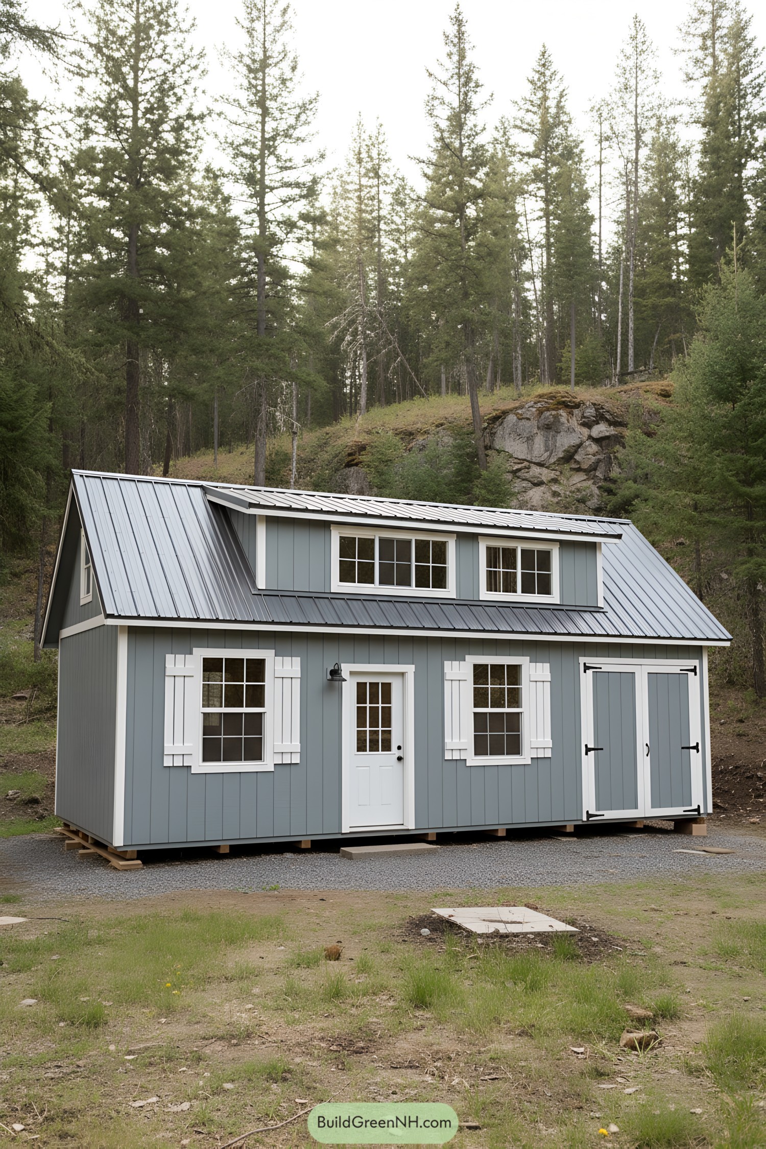 Blue-gray shed house with metal roof, dormers, and white trim in a forest setting
