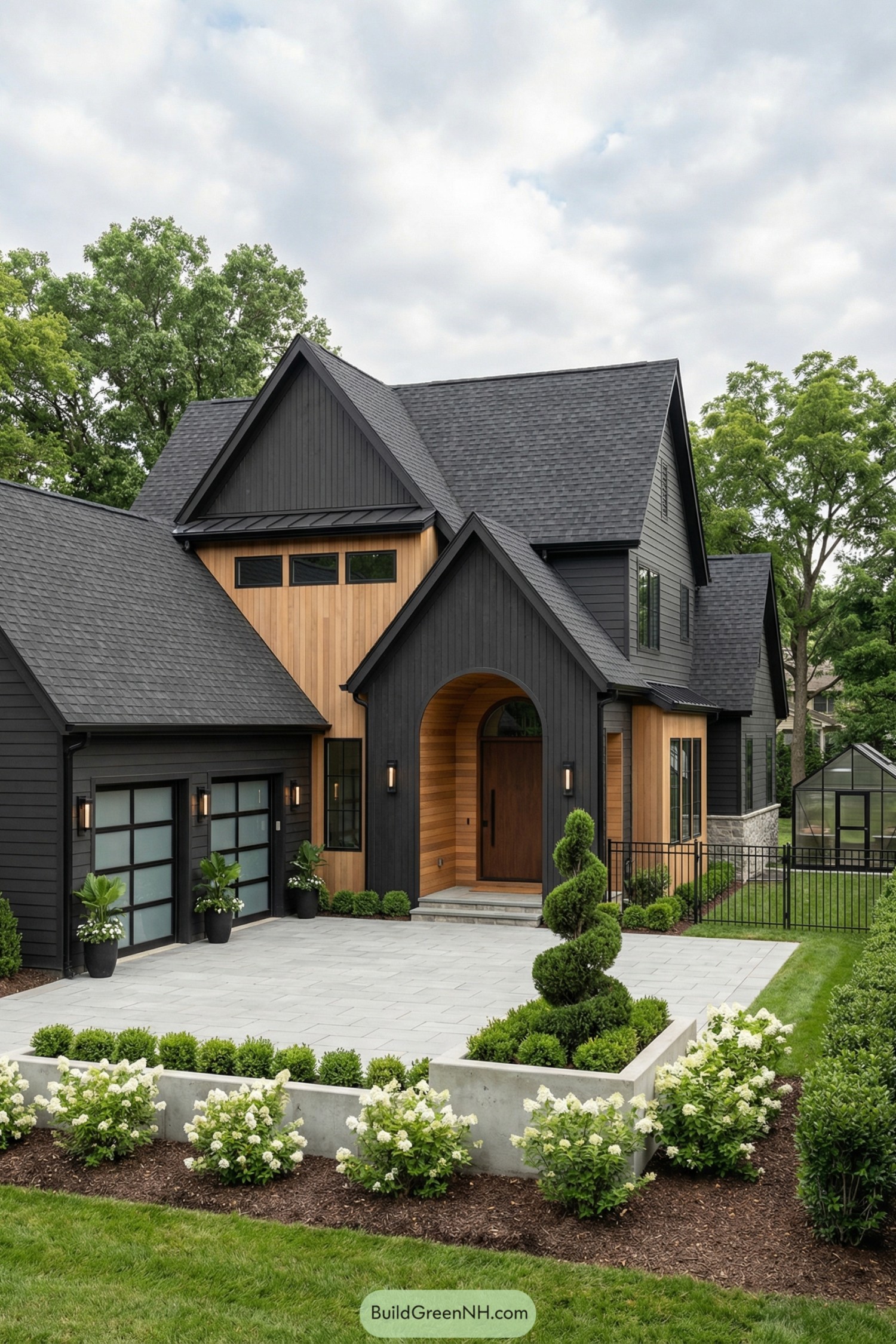 Dark modern cottage with black cladding, cedar accents, and arched entry framed by manicured landscaping