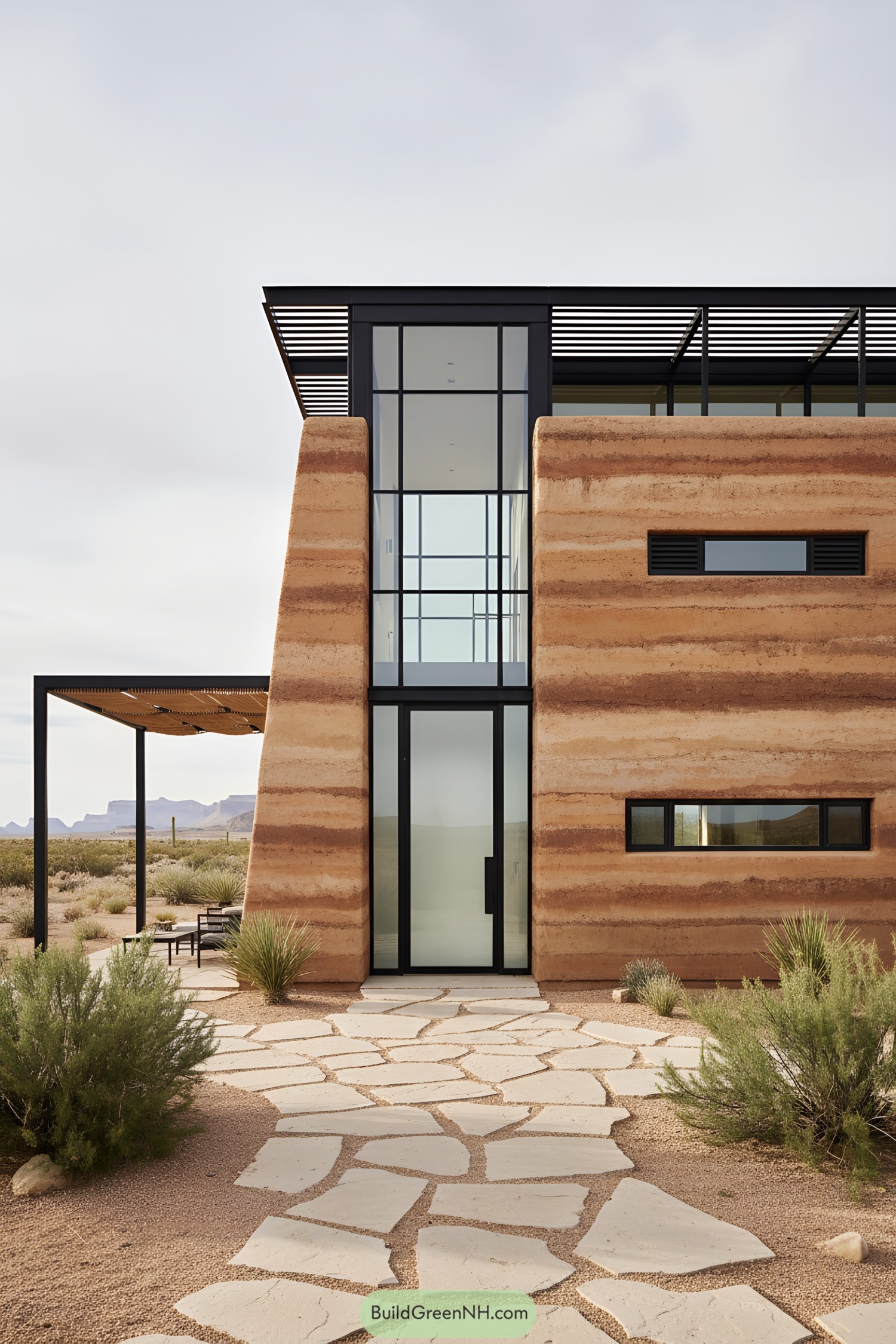 Modern desert house with tall glass atrium framed by rammed earth walls and slim metal pergola