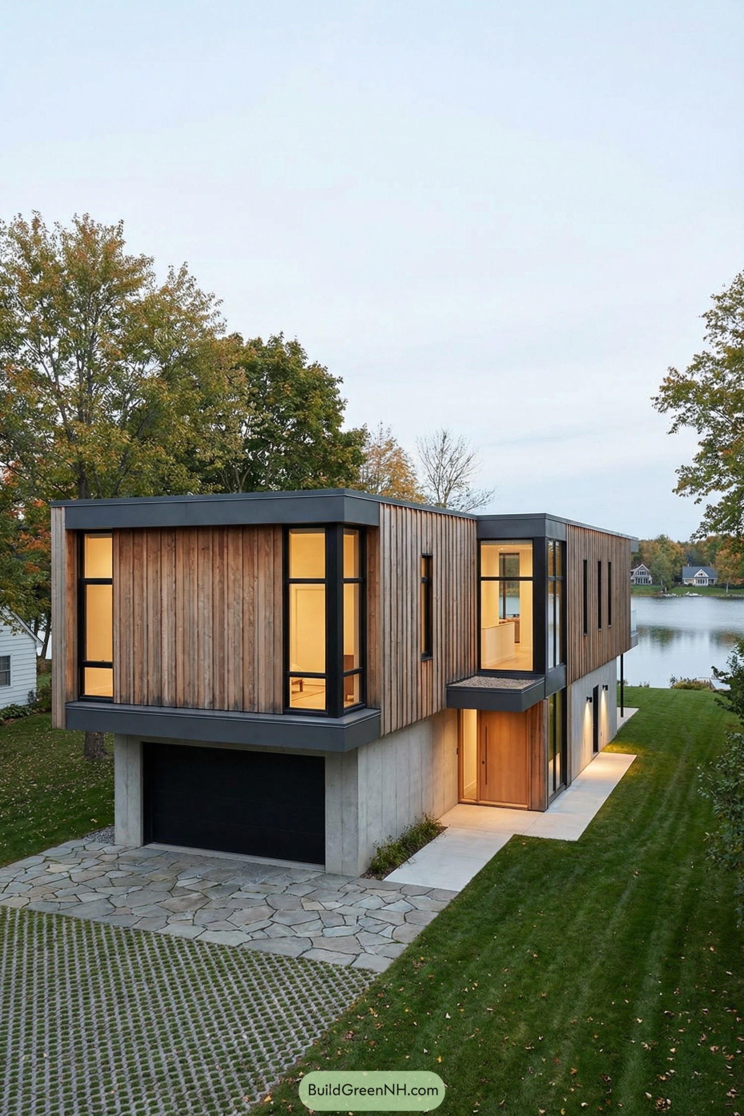 Two story modern house with wood cladding, large windows, and concrete base overlooking a calm rural lake