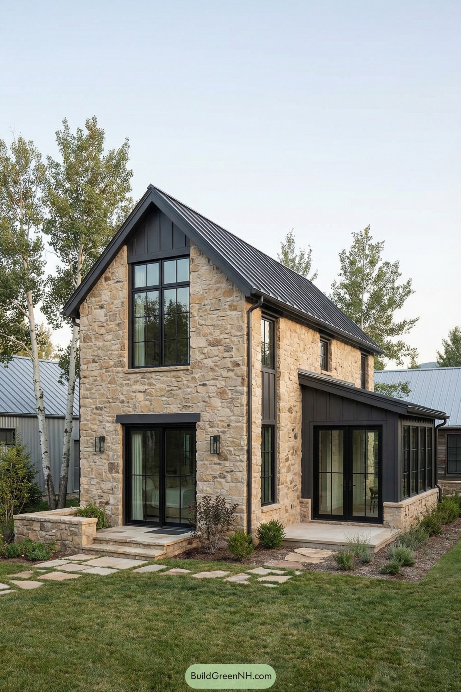 Modern stone cottage with tall black windows and metal roof. Mix of limestone walls, dark trim, and glassy sunroom