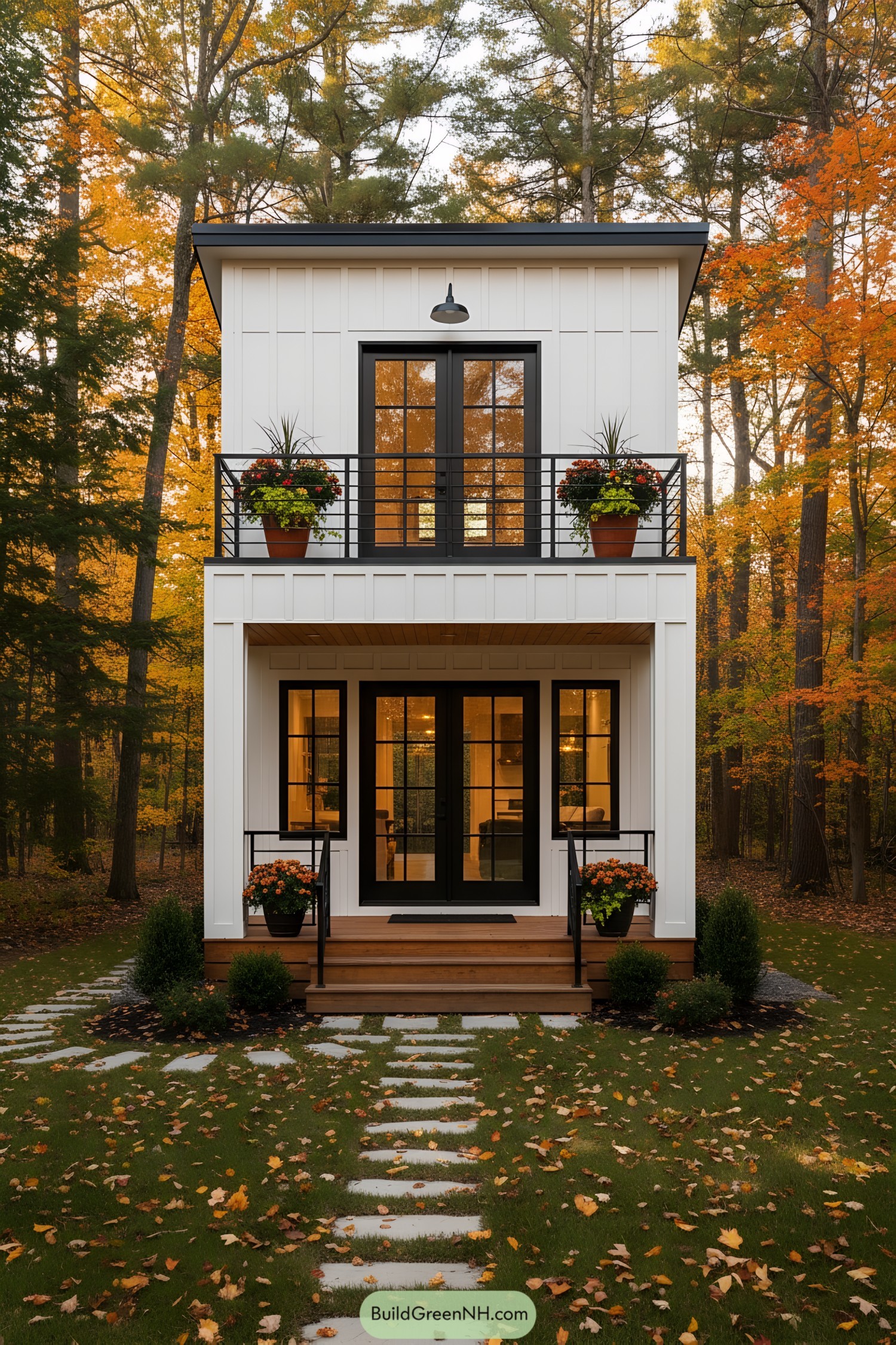 Compact white two-story tiny house with black-framed doors and balcony railings set in autumn woods