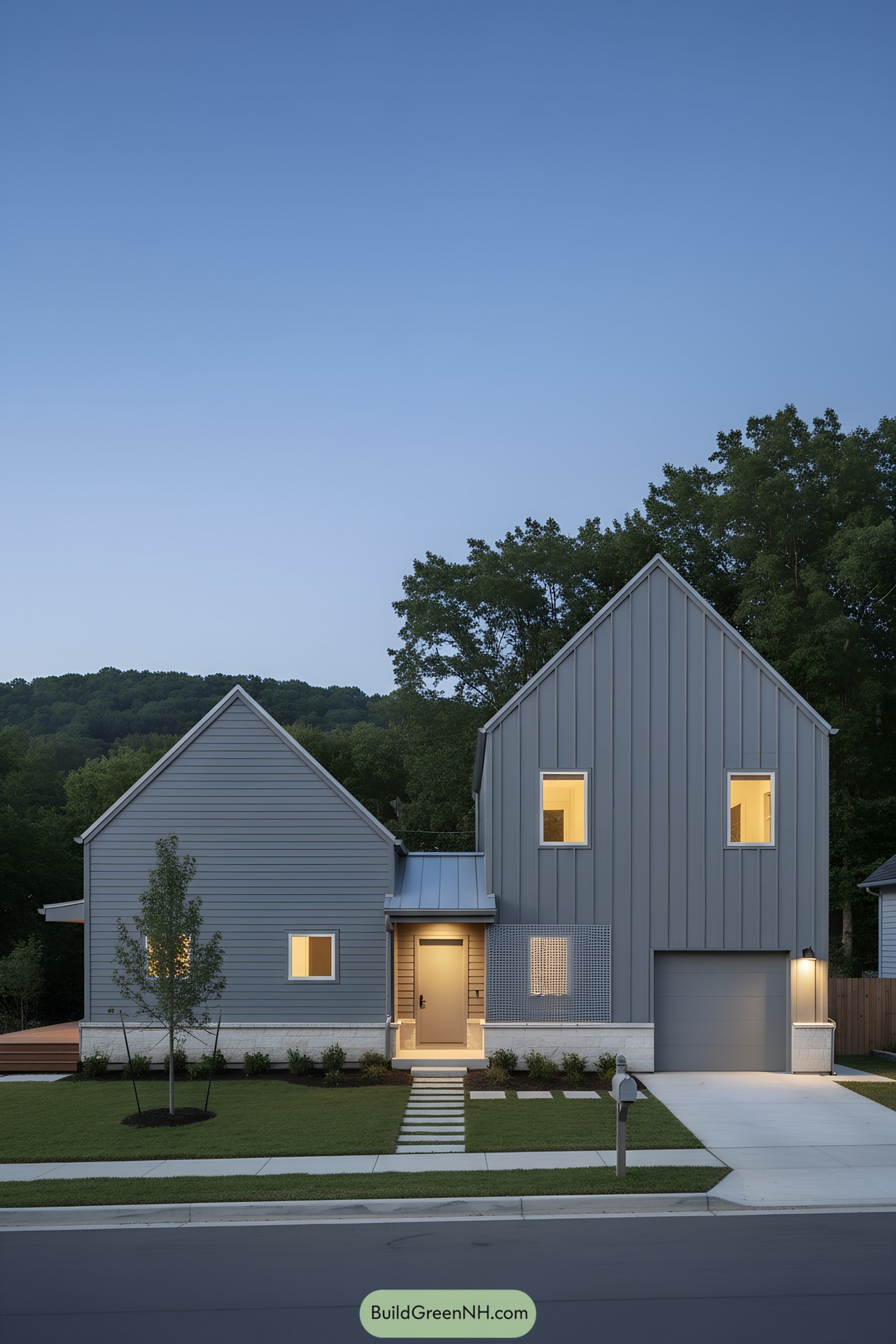 Modern gray gabled house at dusk with warm windows and neat lawn