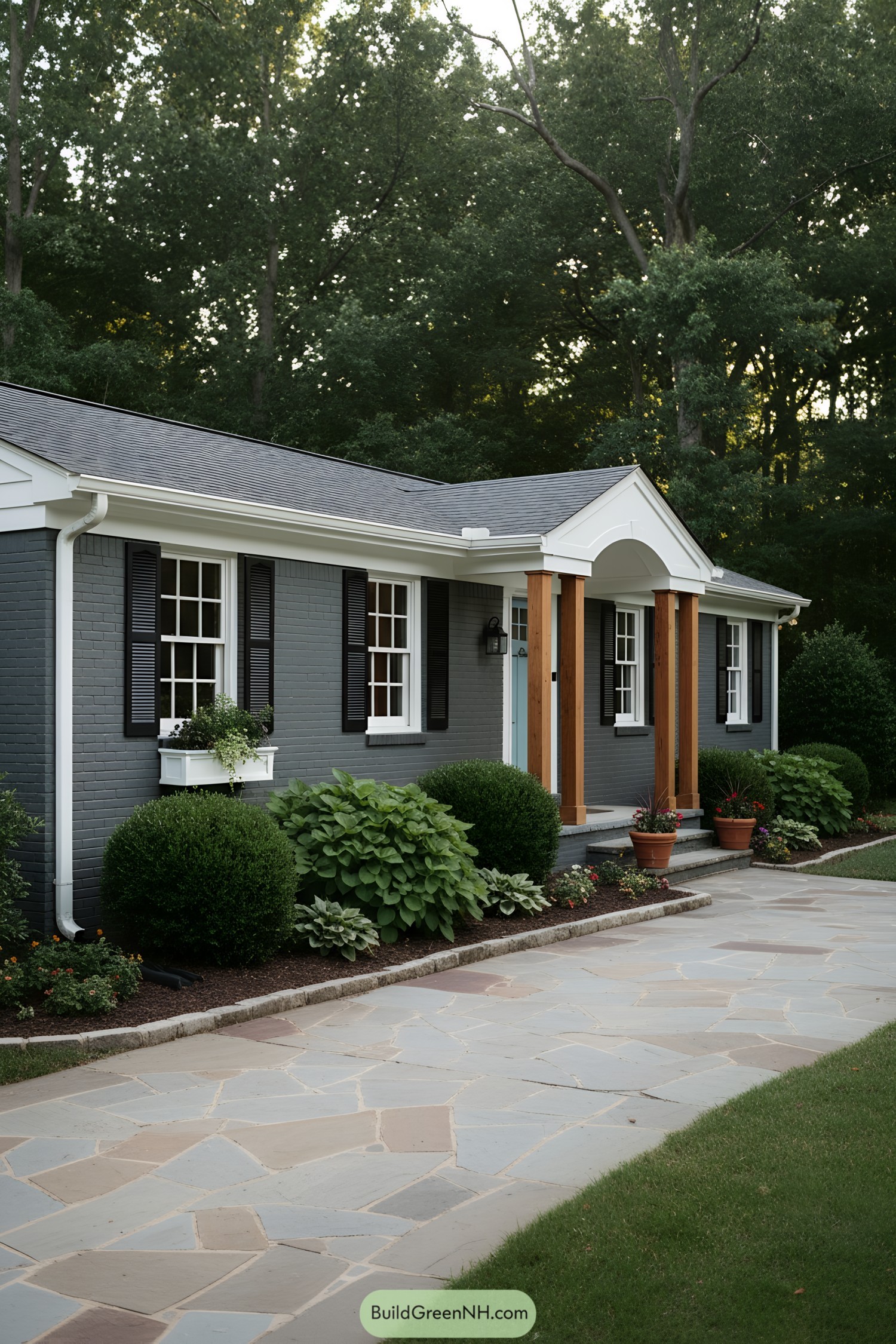 Gray-painted ranch with white trim, black shutters, and warm wood porch posts; tidy shrubs line a flagstone walk. Arched portico and window box add charm