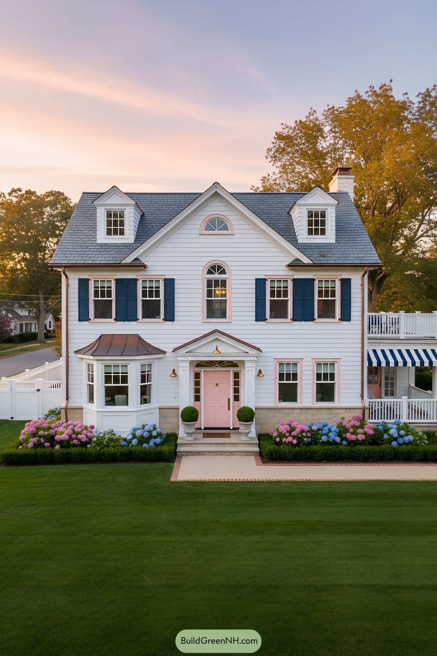 White clapboard house with pink door, navy shutters, copper accents, and striped side awning