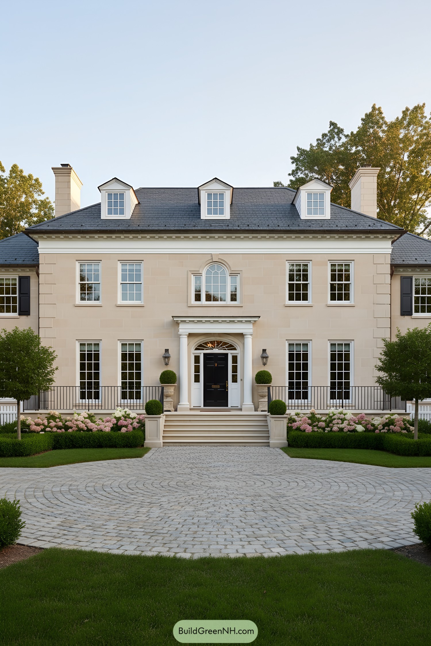 Symmetrical beige manor with black door, dormers, and manicured landscaping