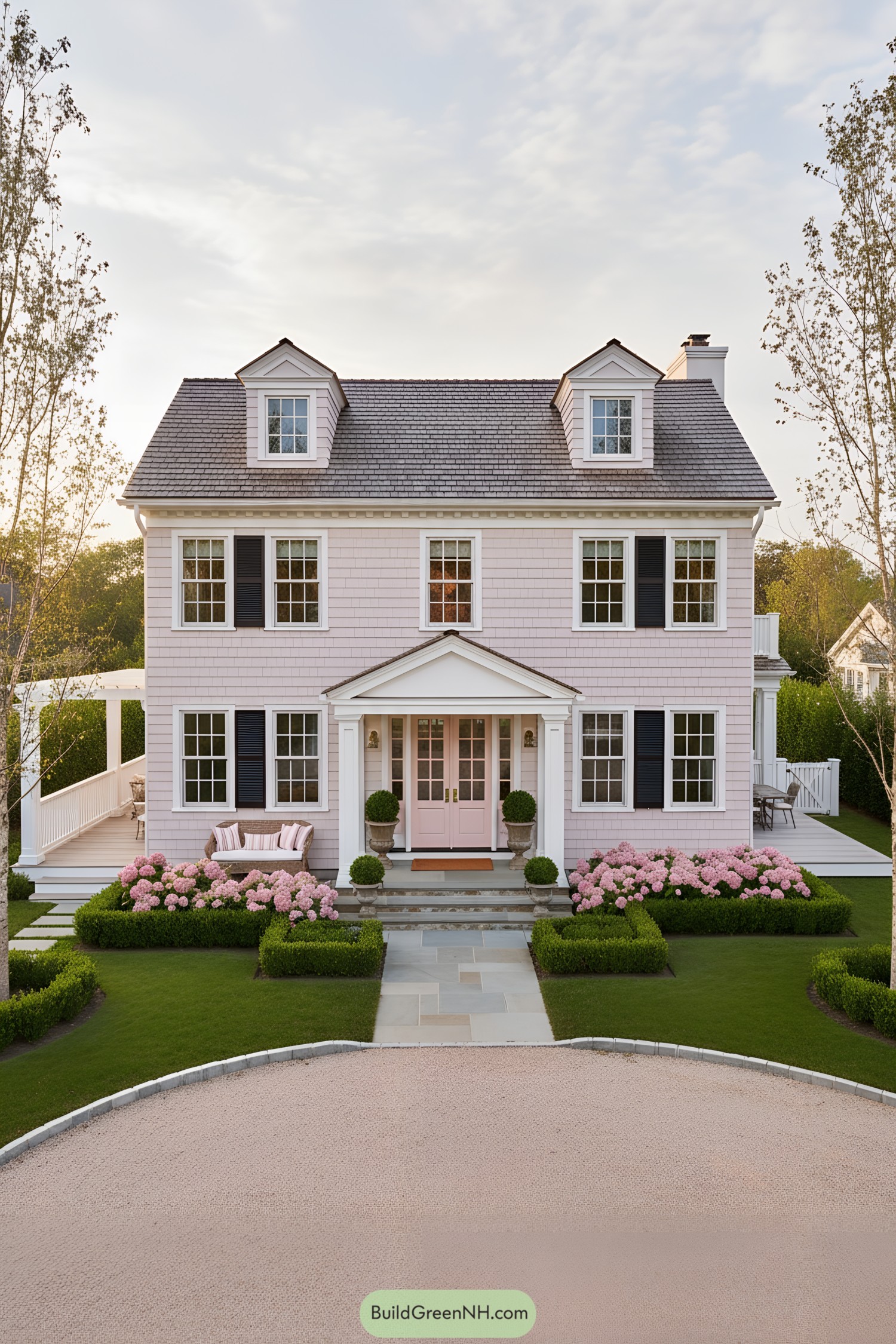 Pale pink shingle Colonial with black shutters, dormers, and manicured hydrangea beds