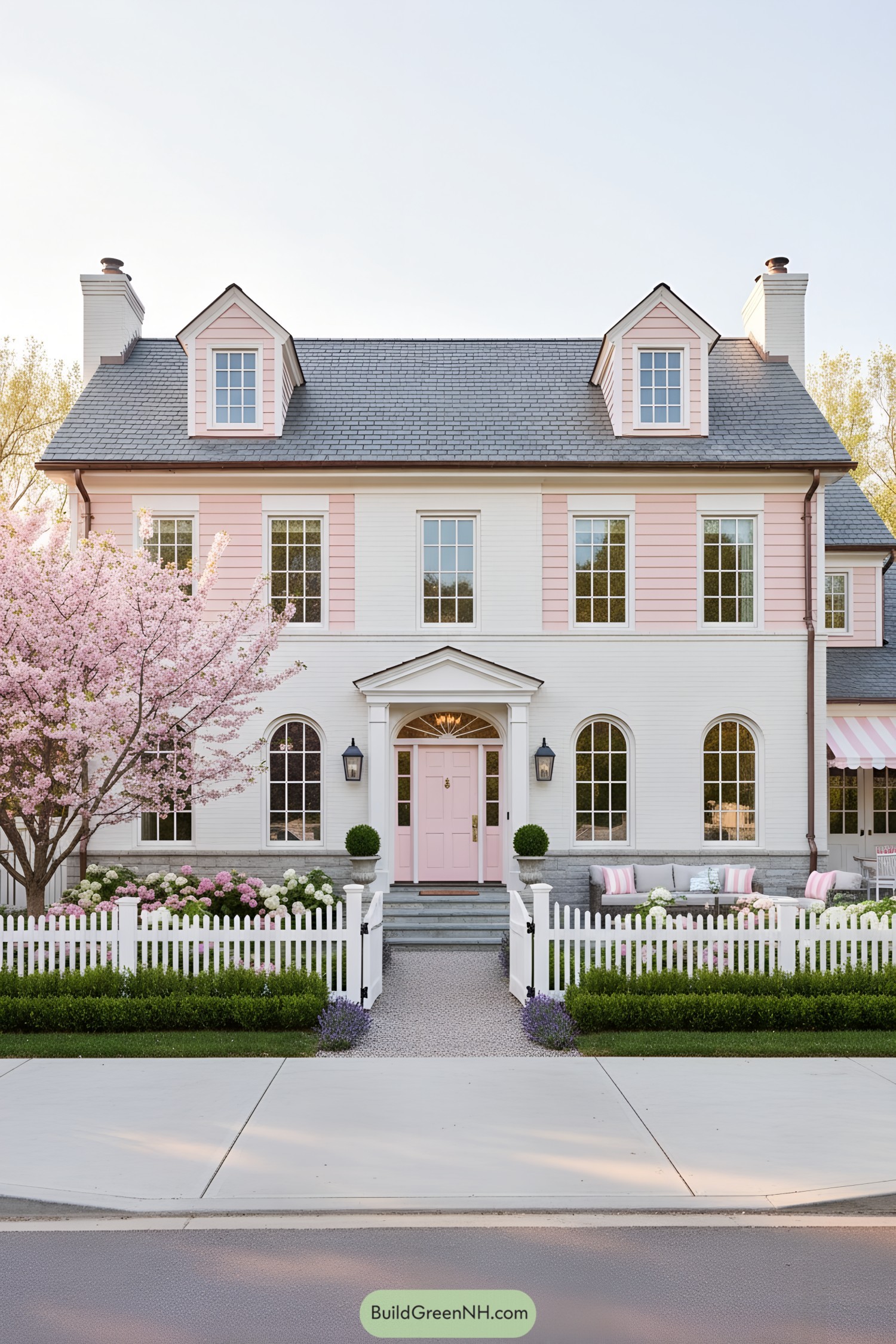 Pale-pink colonial with dormers, picket fence, and striped awning