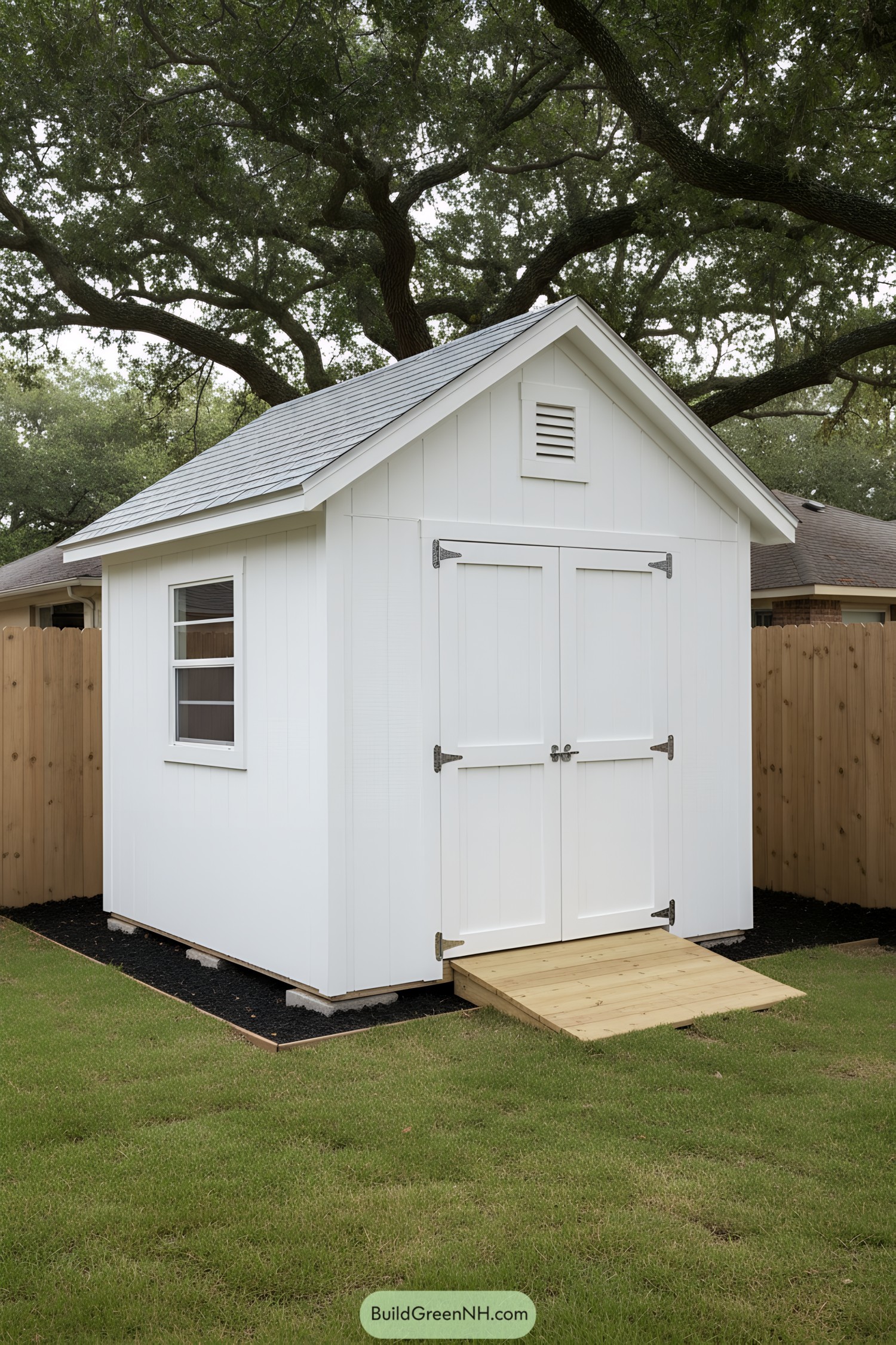 Small white gable-roof shed with loft doors and a wood ramp in a fenced yard