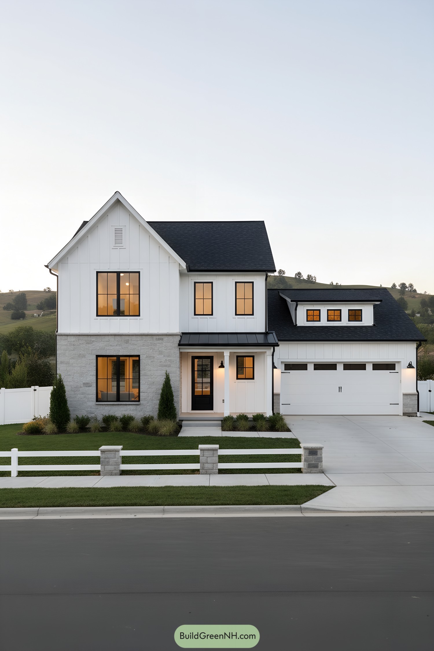 White farmhouse with black roof and warm lit windows, stone base, and attached garage