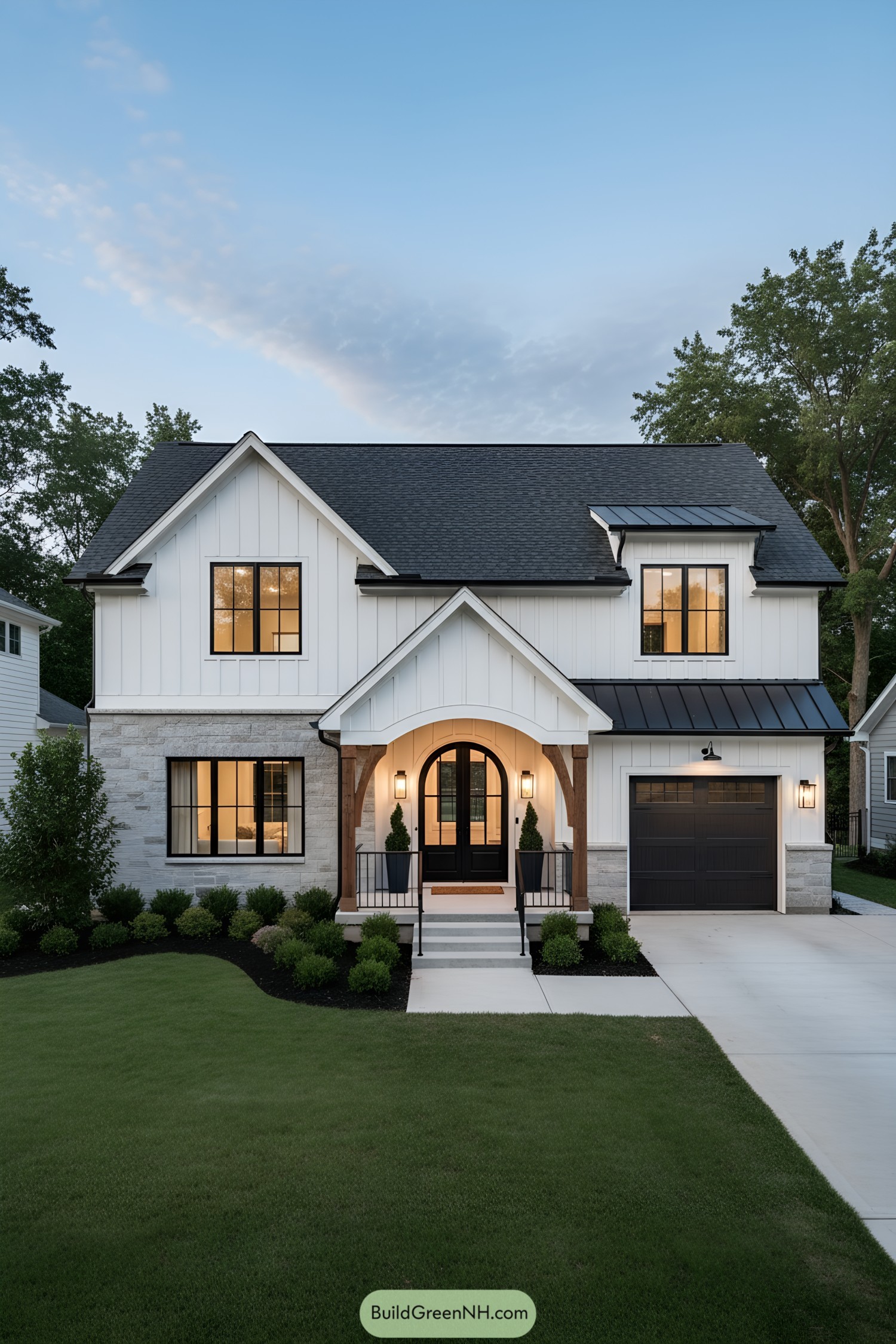 White board-and-batten farmhouse with arched porch, black windows, and attached garage at dusk