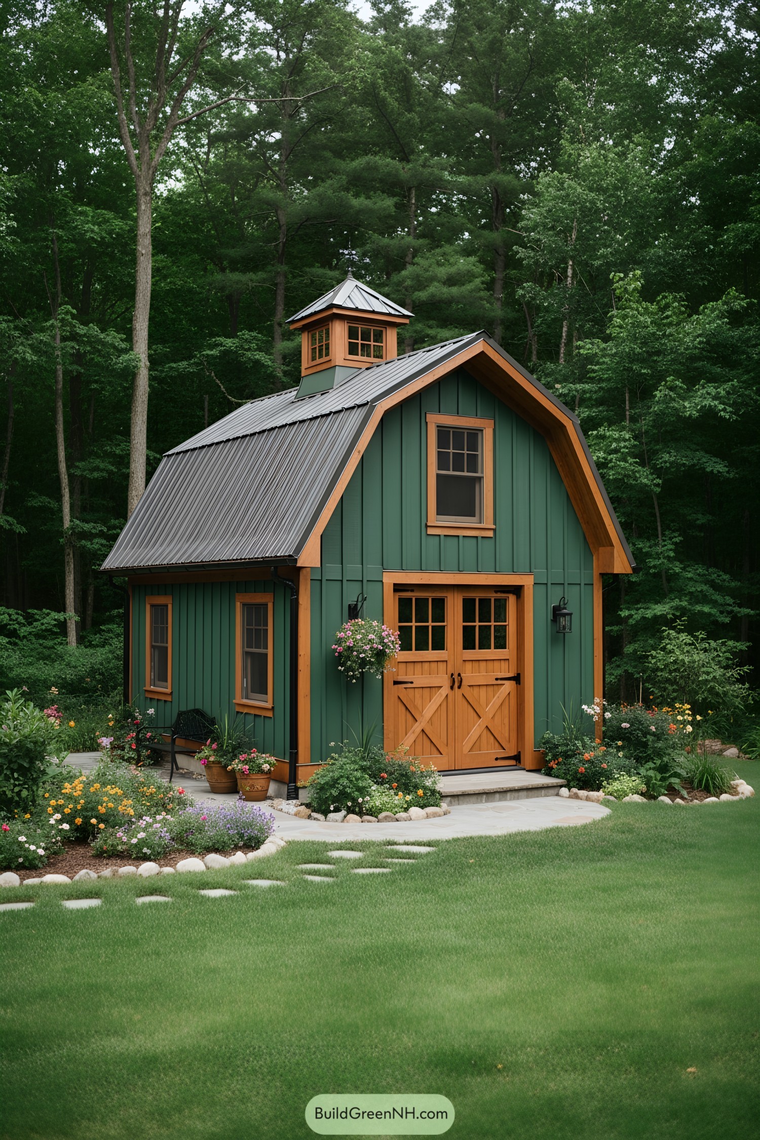 Green mini barn with copper-tone trim and cupola in a flowered yard