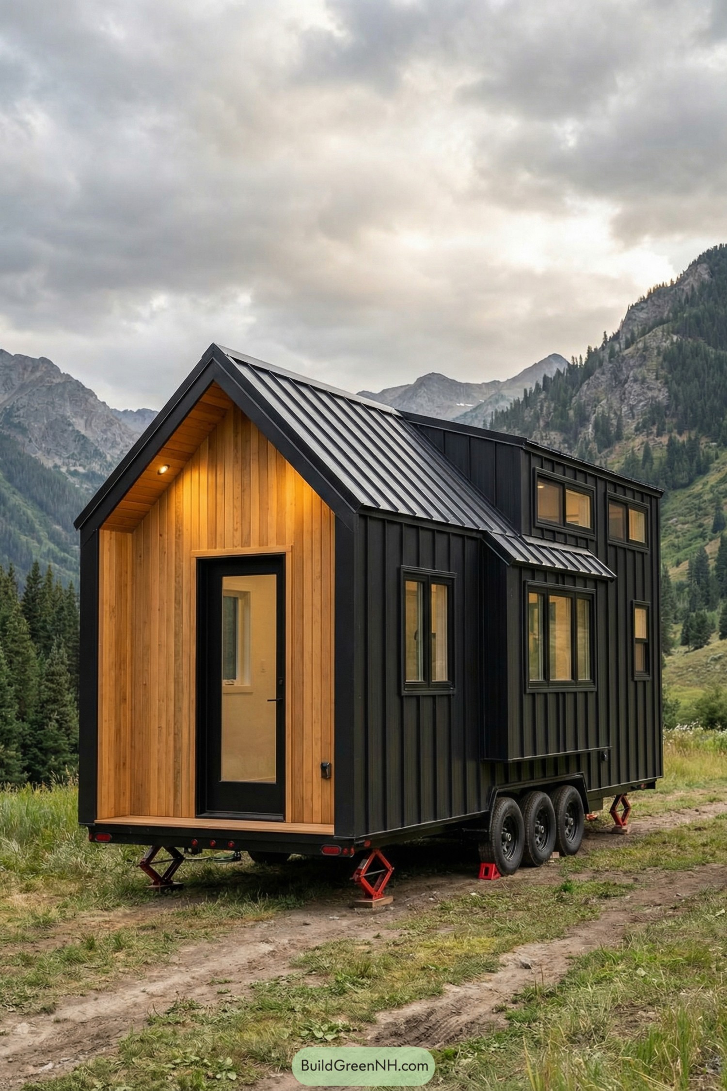 Tiny house with black metal siding, cedar entry, and gabled roof set in mountains