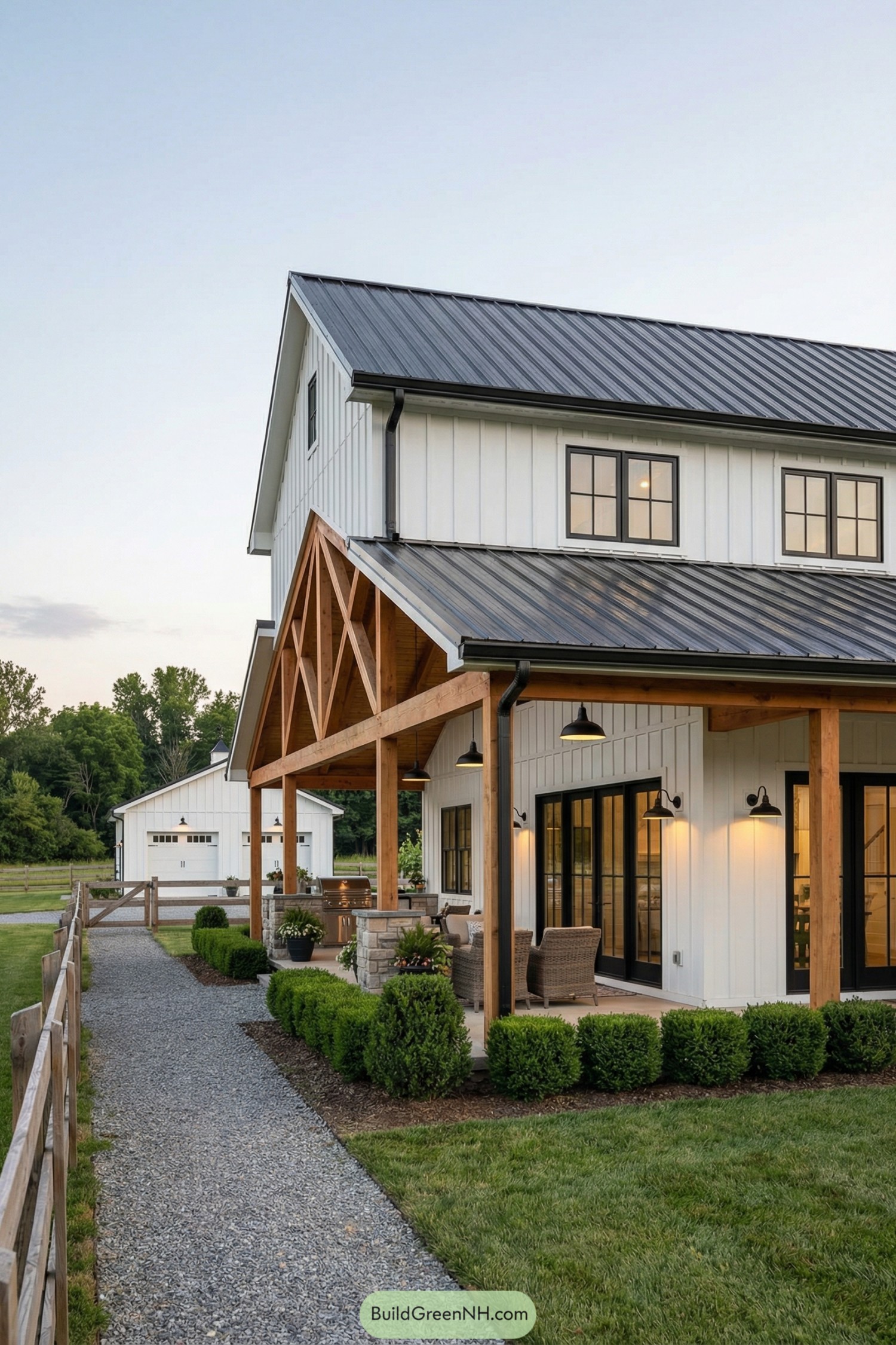 White board-and-batten barnhouse with black metal roof and timber truss porch at sunset