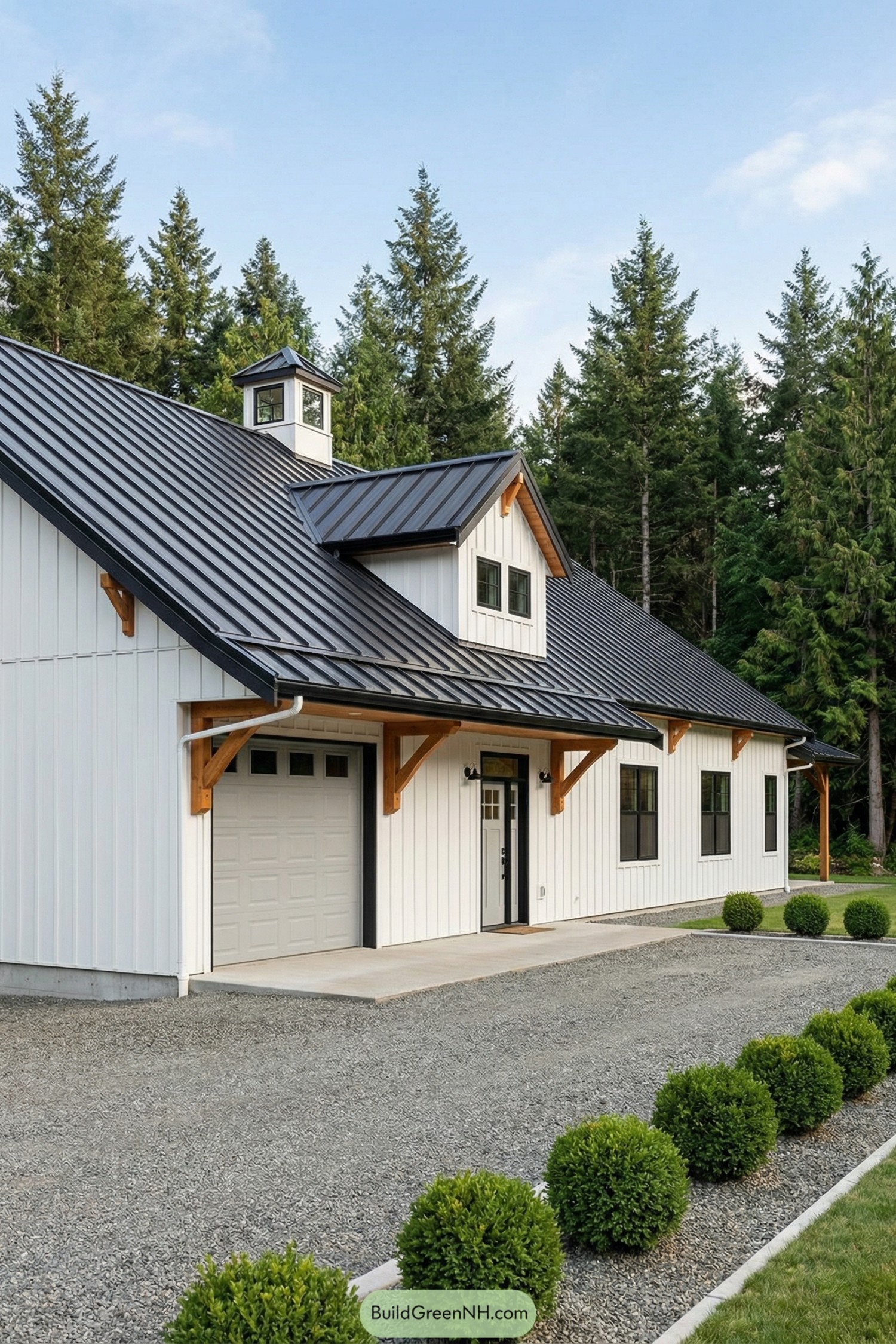 White board-and-batten barn home with black metal roof, dormer, and timber brackets beside a gravel drive