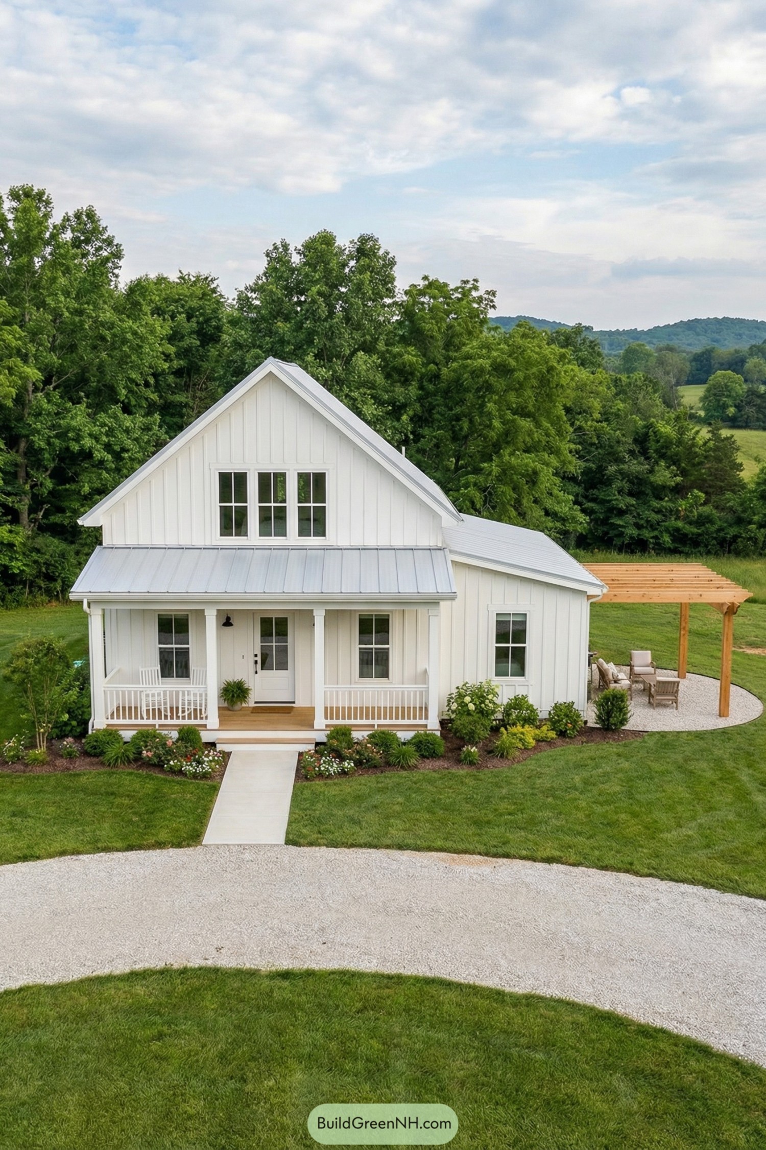White board and batten farmhouse-style tiny cottage with front porch and side pergola seating area on a green country lot