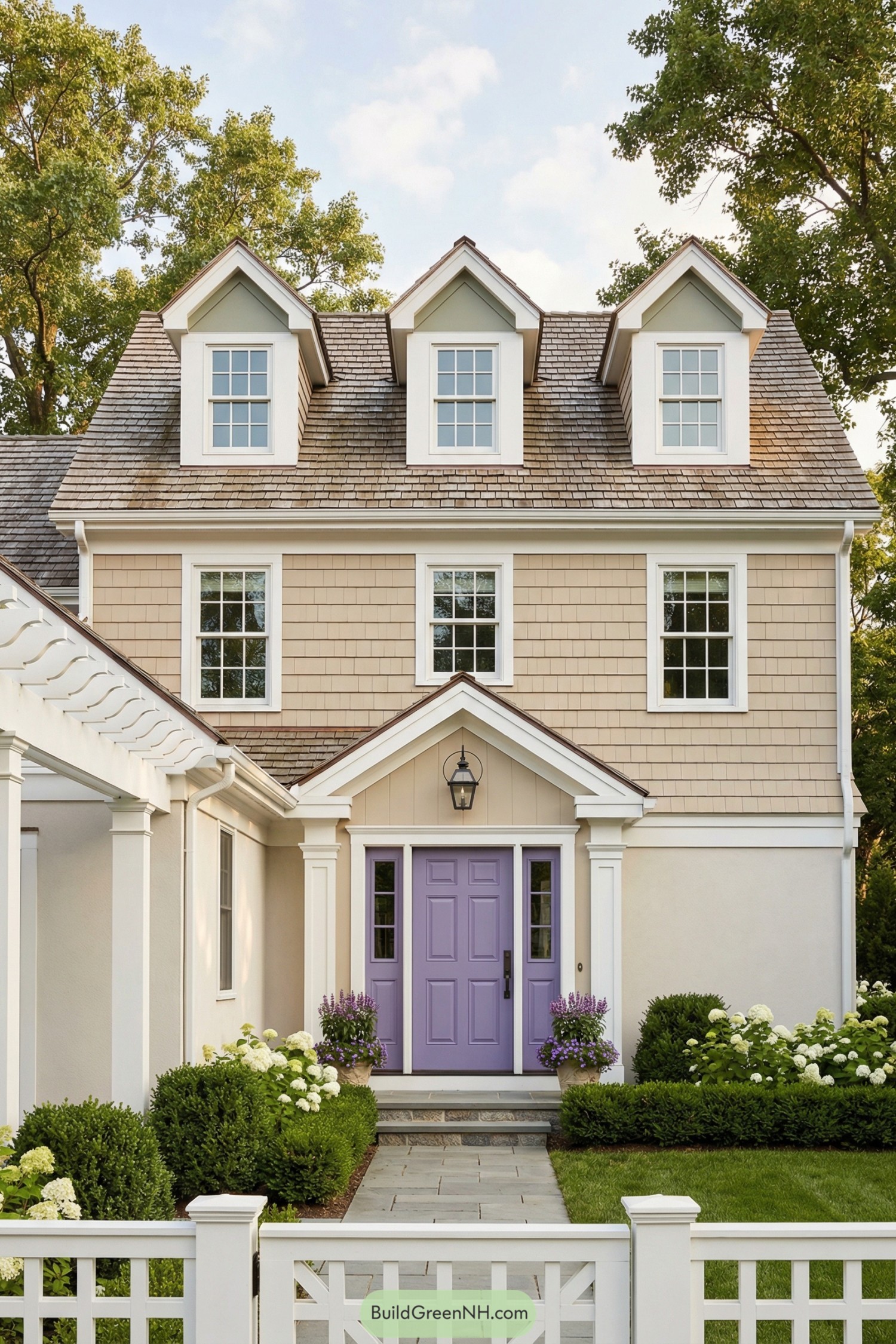 Beige two-story house with dormers and lilac front door framed by lush shrubs