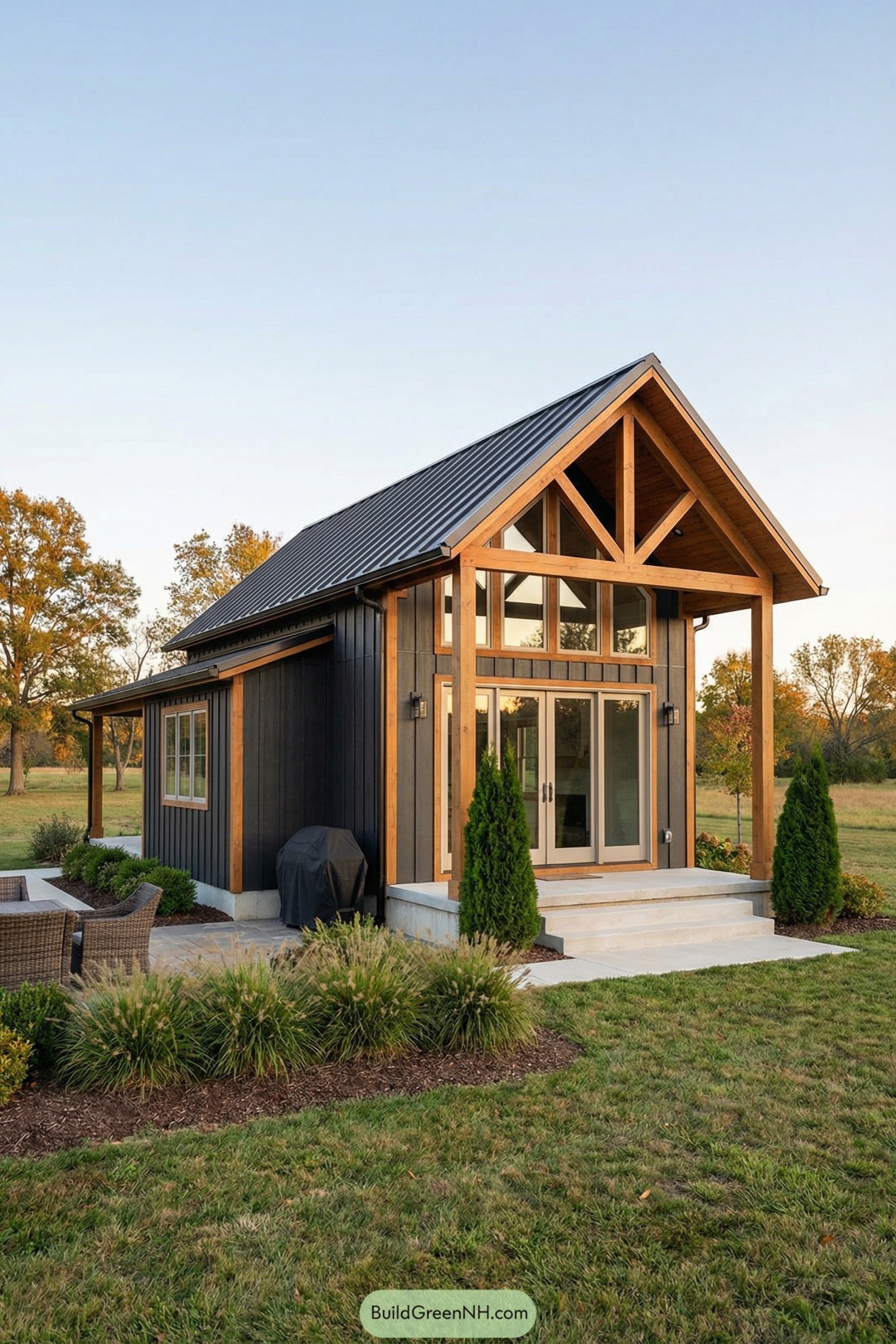 Compact black-and-wood barndominium with tall gabled entry and patio in open field