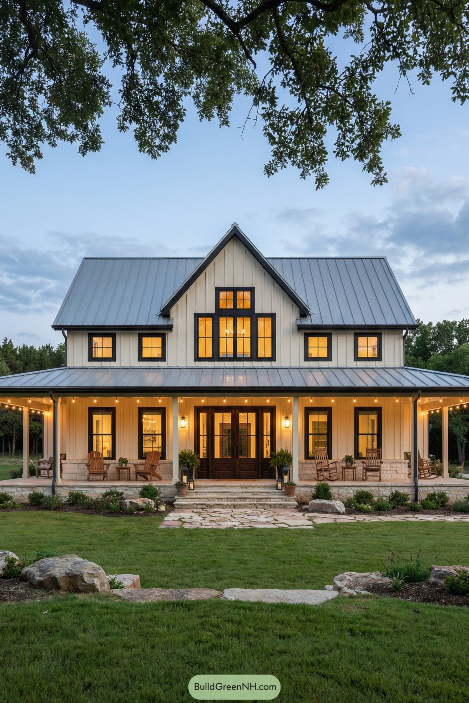 Two-story cream board and batten barndominium with metal roof and wraparound porch at dusk