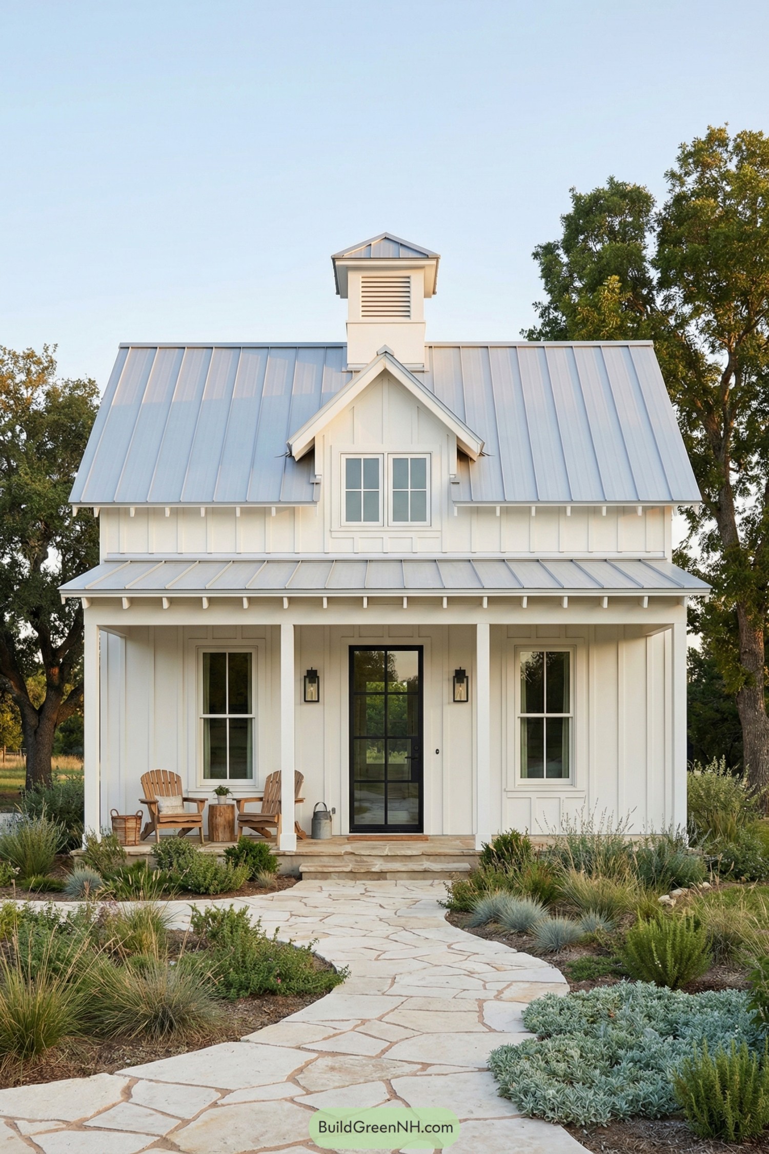 White board and batten cottage with metal roof, front porch, and stone path through native landscaping