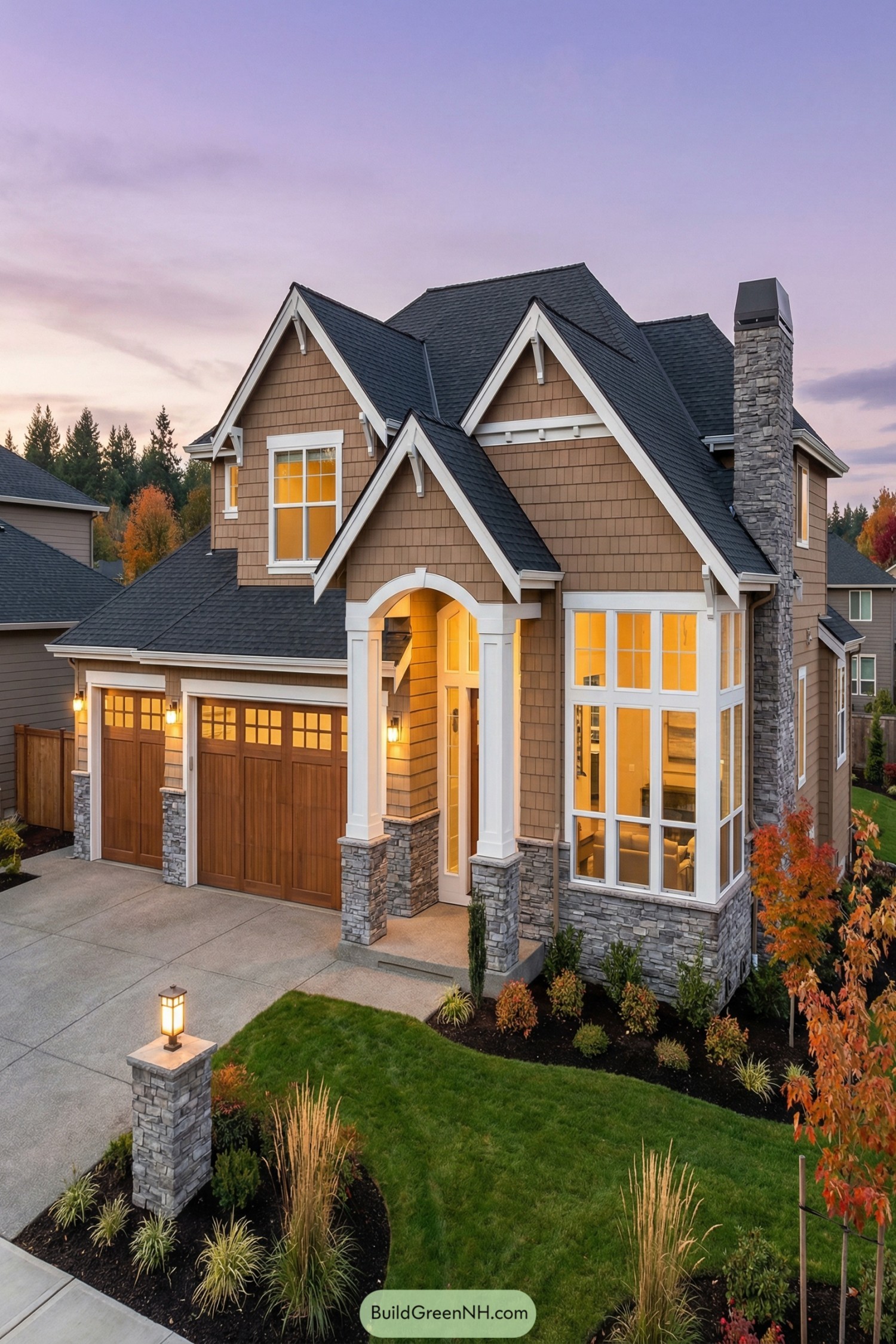 Two story craftsman style house at dusk with stone accents wood garage doors and warm interior lights
