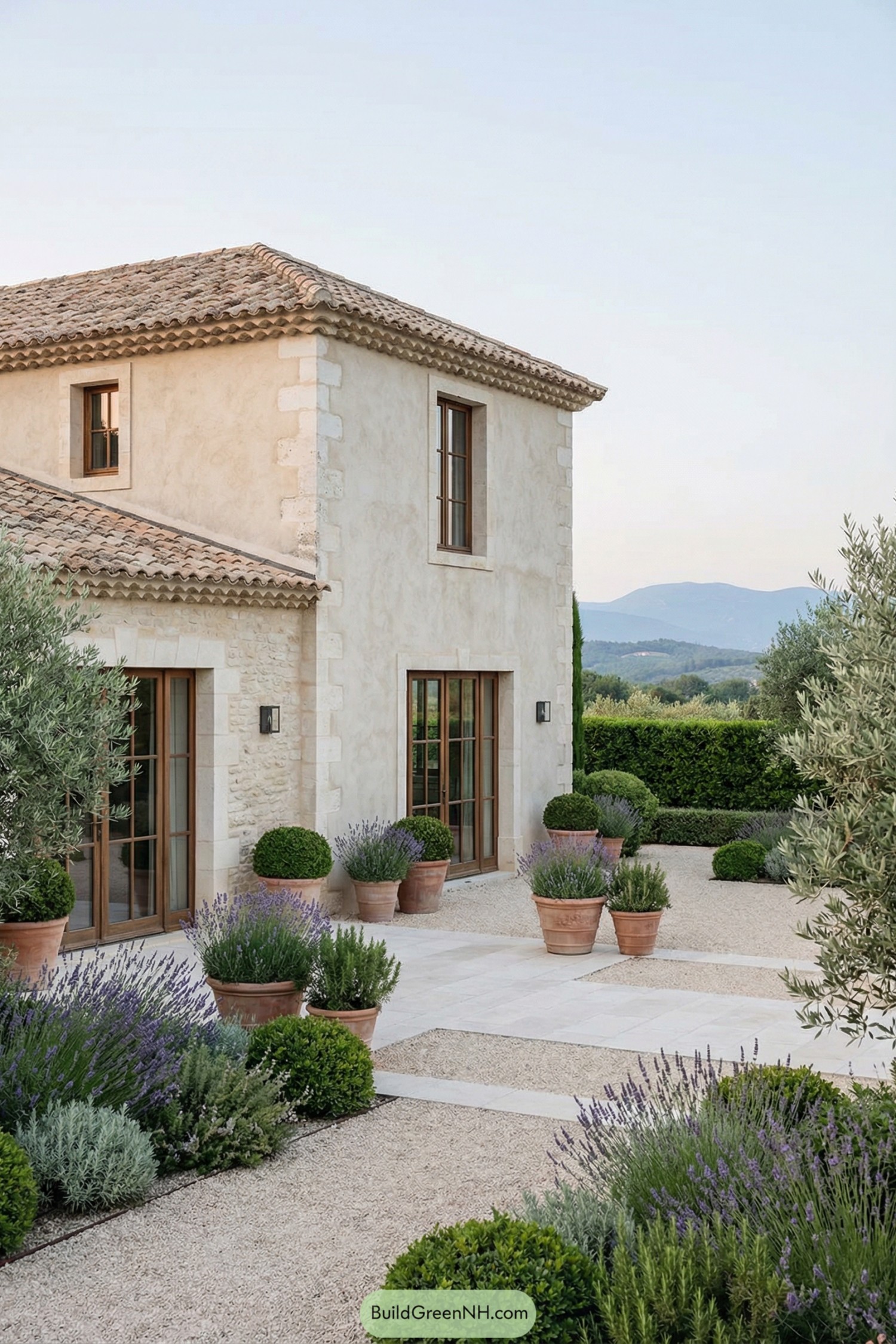 Rustic French courtyard with gravel paths, terracotta pots, lavender, and a pale stone farmhouse overlooking distant hills