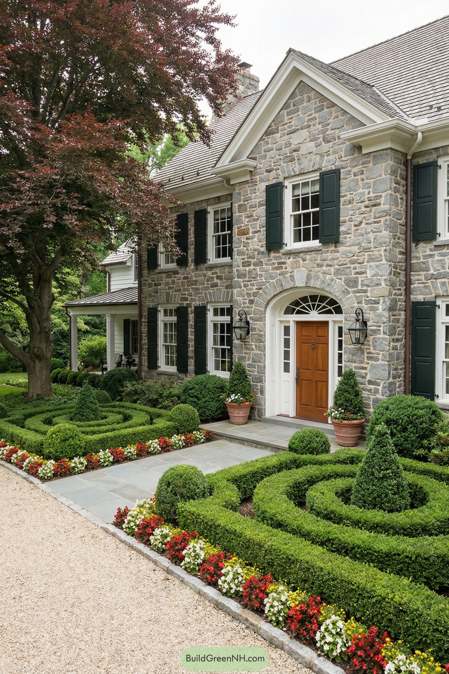 Stone-front house with formal boxwood parterre, gravel drive, and colorful flower borders