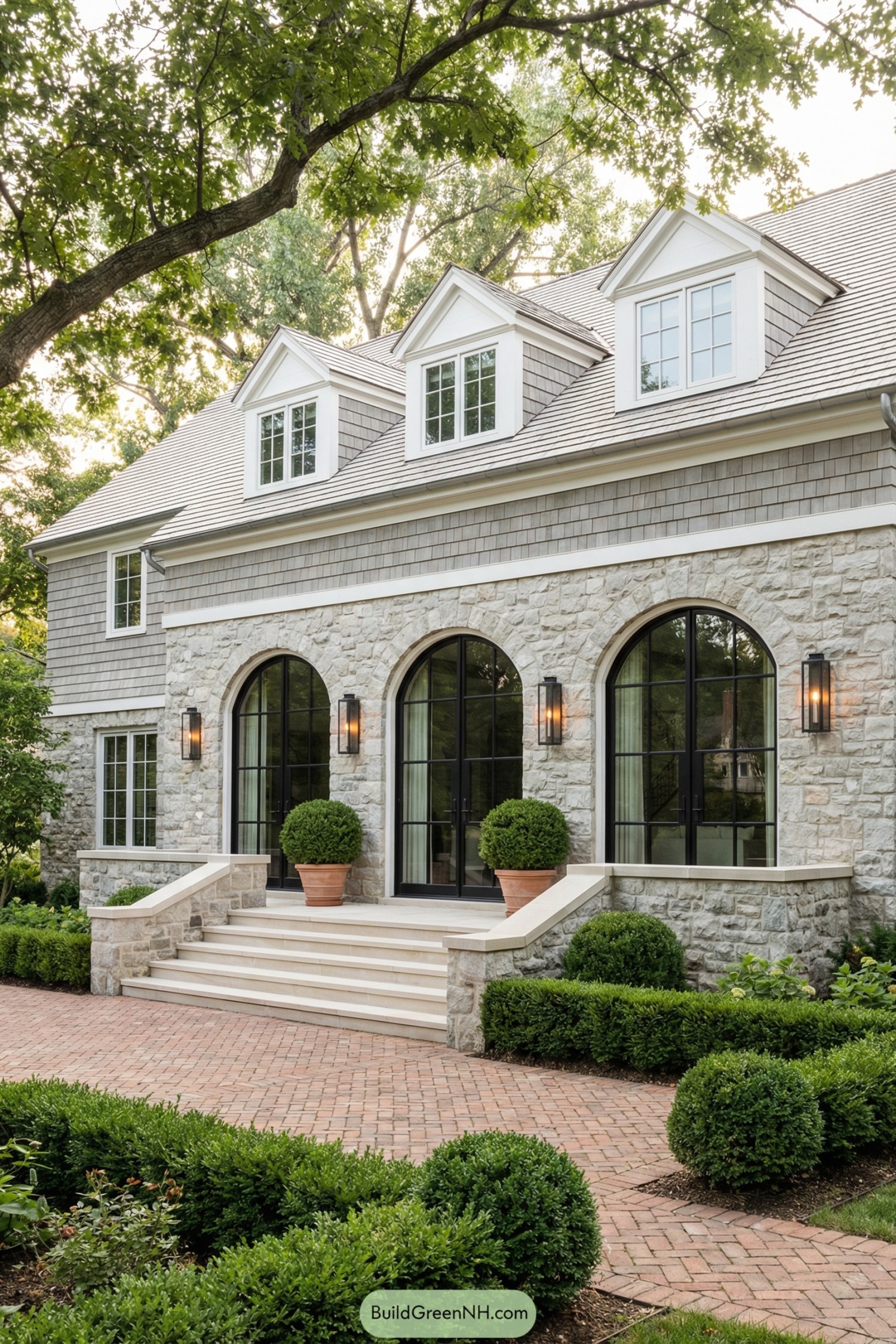 Elegant stone house with three large arched black-framed windows, wide front steps, and manicured shrubs