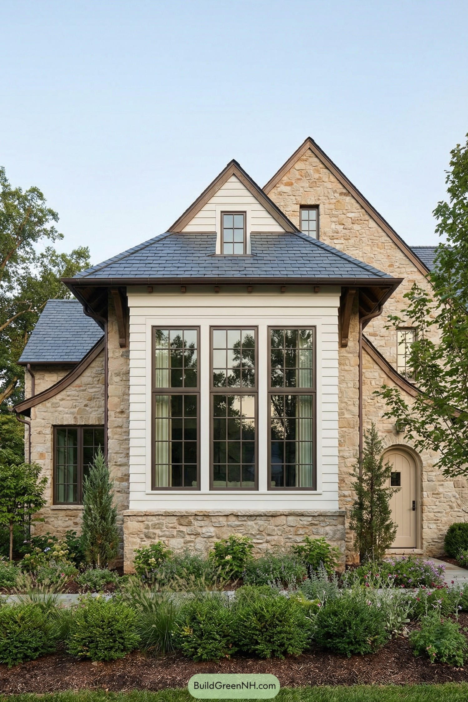Stone-clad house facade with large vertical bay windows and lush front landscaping