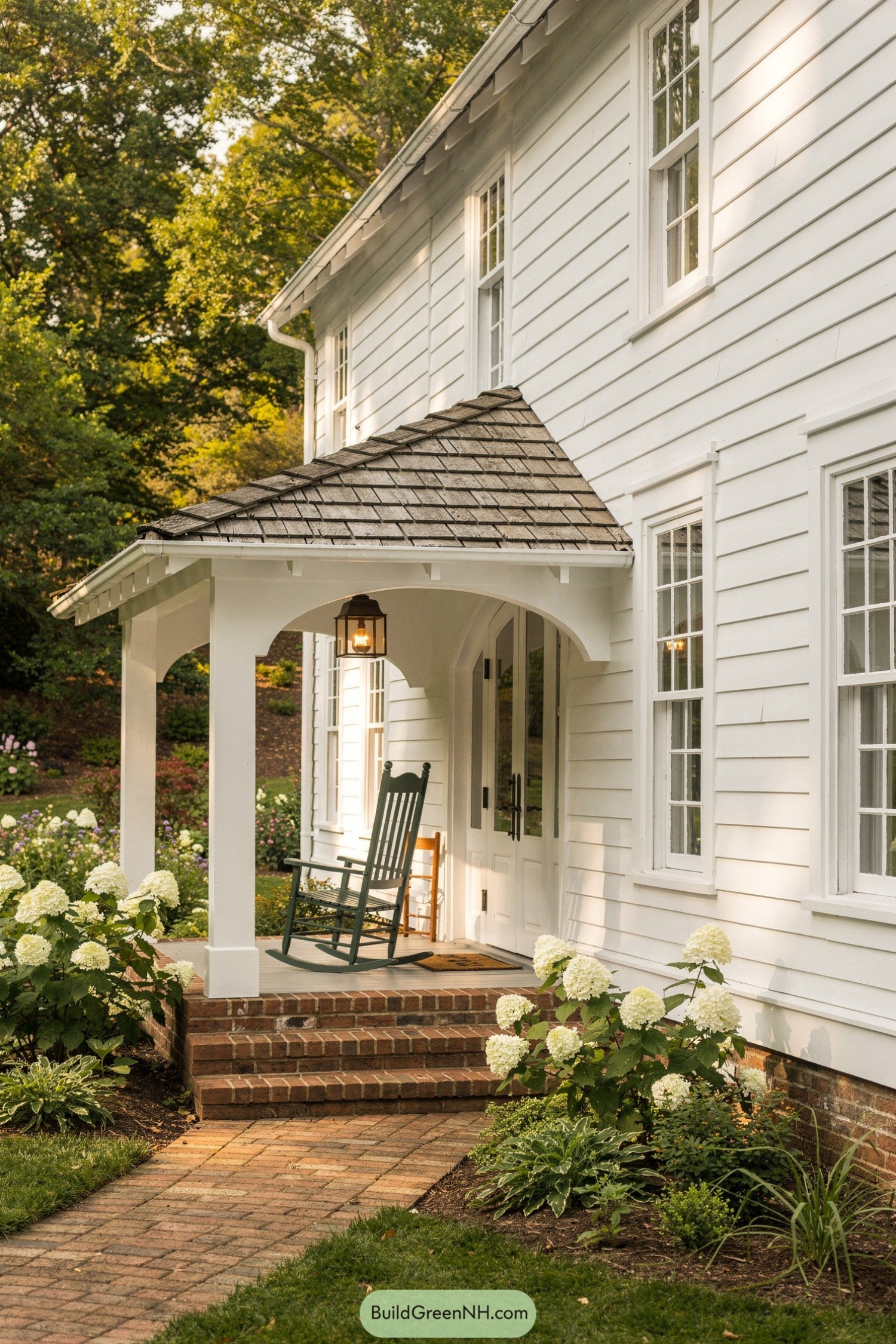 White shiplap house with small covered porch and brick steps framed by blooming hydrangeas