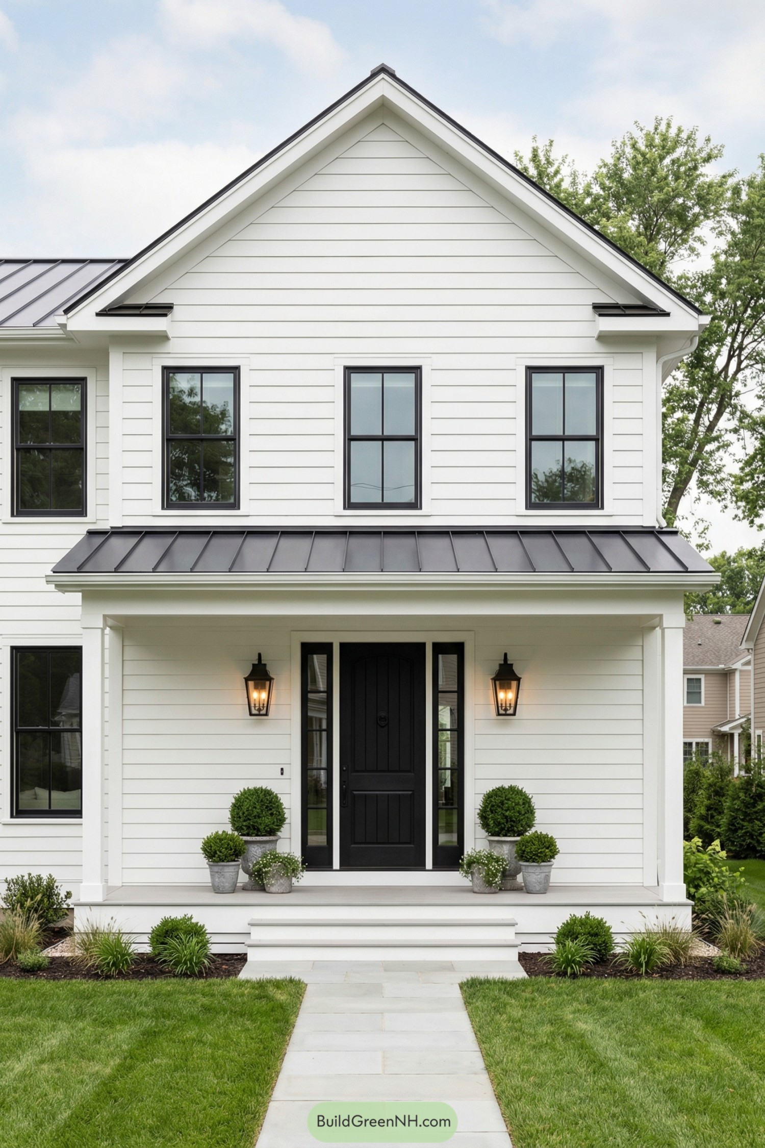 White shiplap house with black door and windows flanked by potted greenery