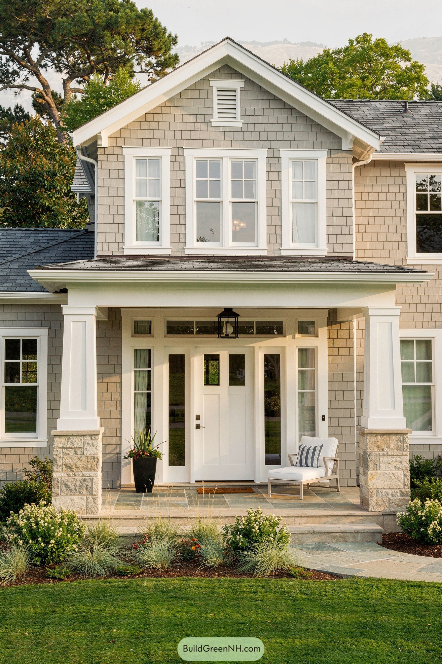 Light gray shingle house with white trim, stone-based porch columns, and a simple landscaped entry