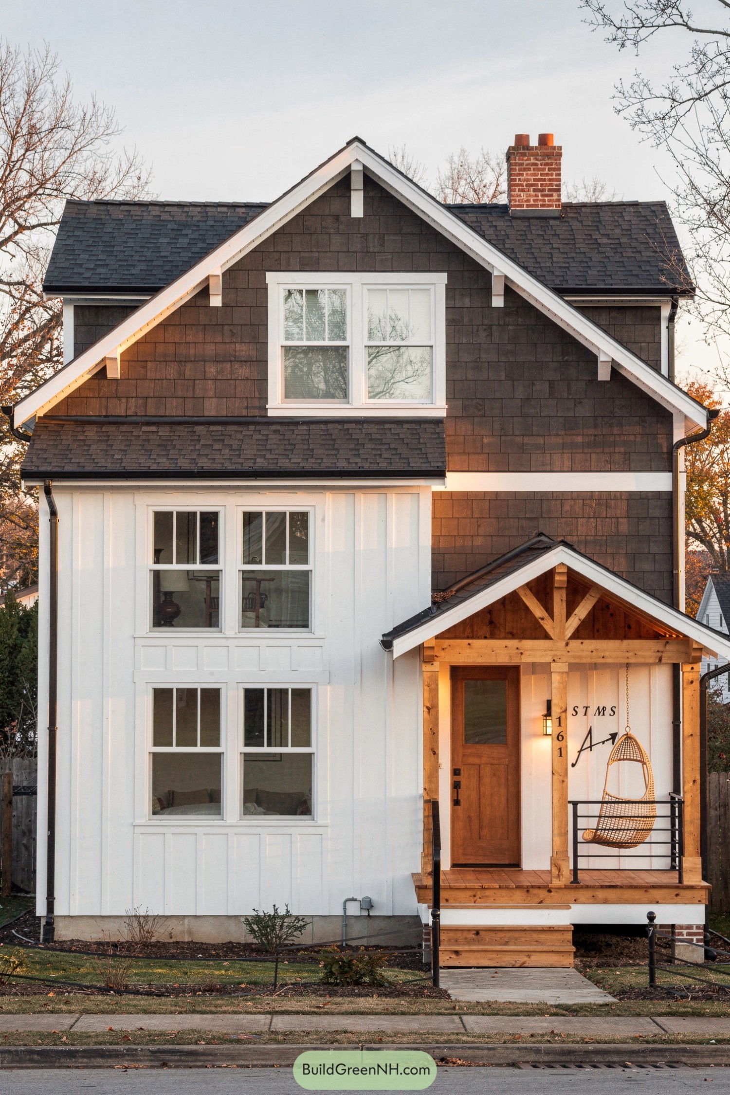 Two-story house with dark shingle upper siding, white board-and-batten lower level, and a warm wood front porch with a hanging chair