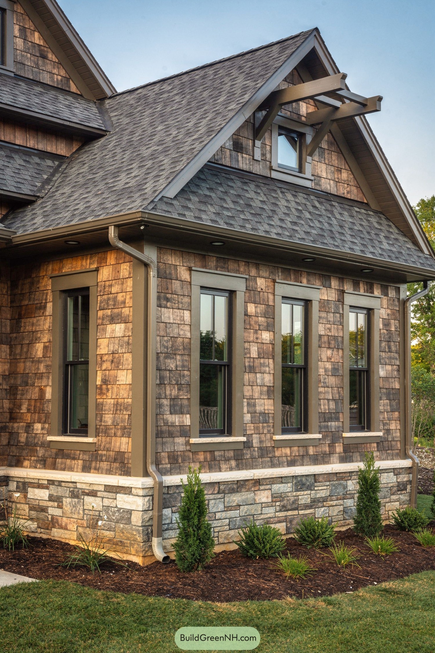 Side view of a shingle house with stone base and gabled roof