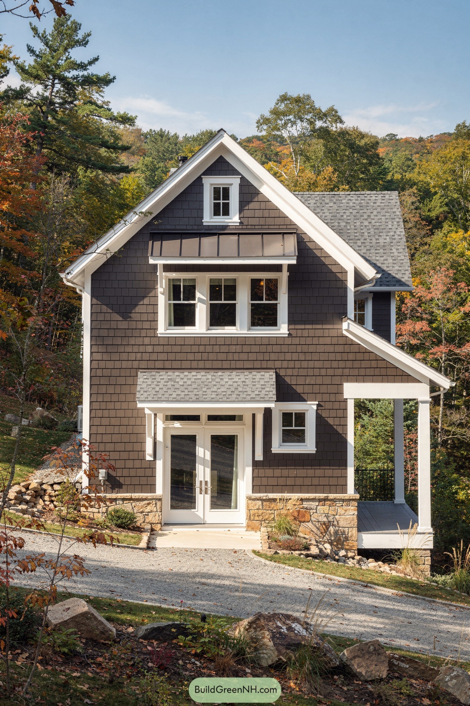 Brown shingle cottage with white trim, stone base, and side porch in a wooded landscape