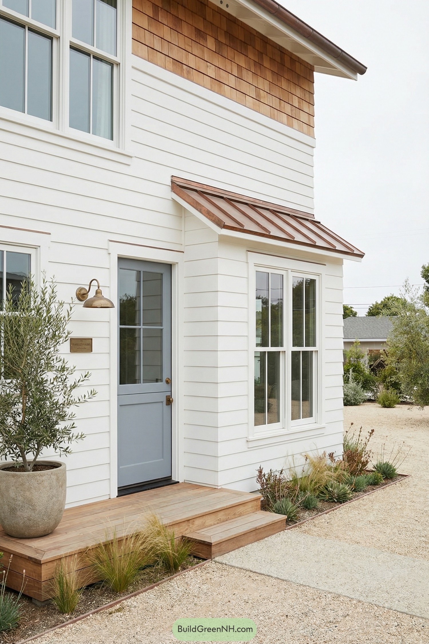 White shiplap house with blue door copper awning and small wood entry deck