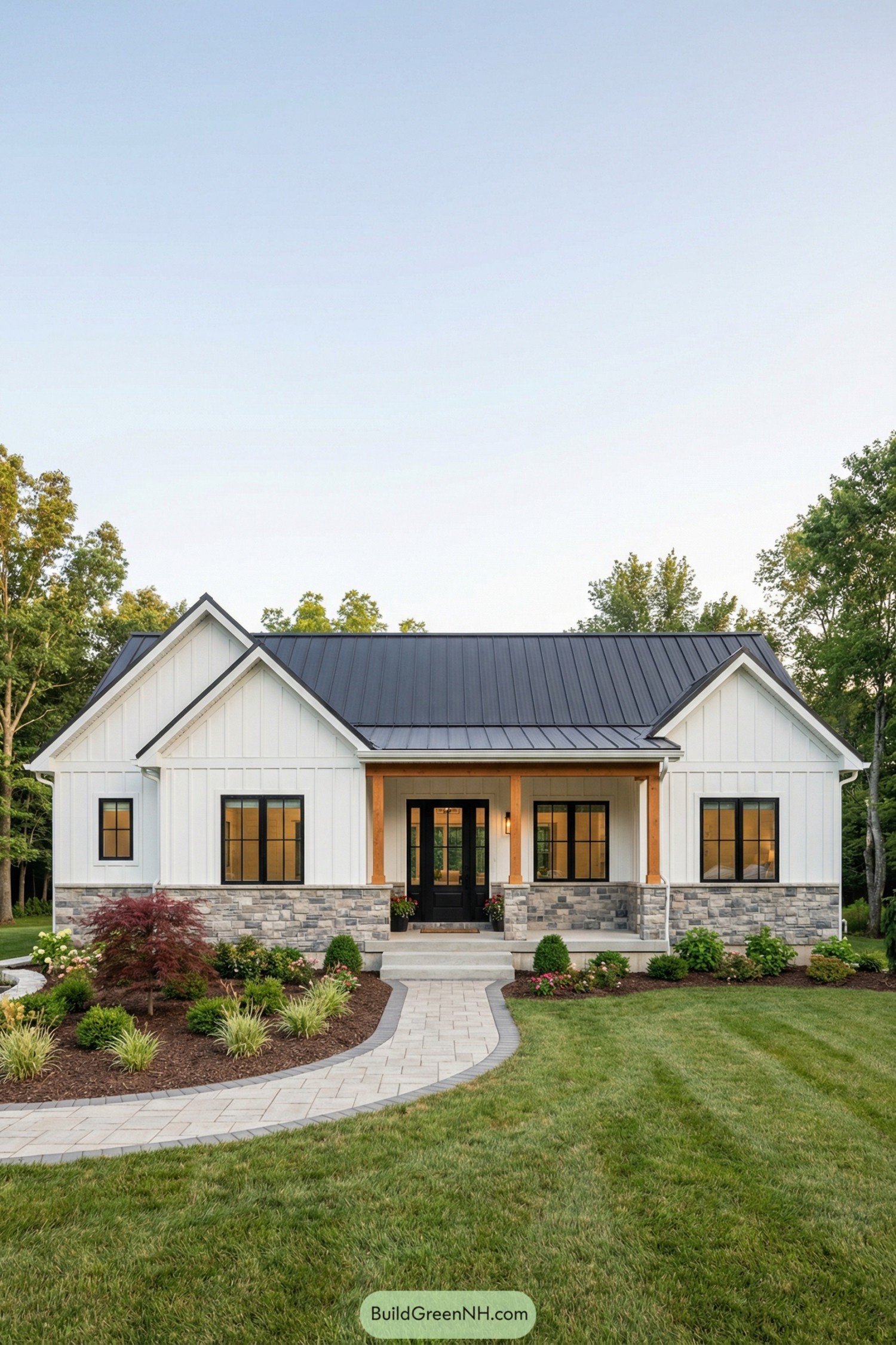 White farmhouse with vertical siding black metal roof stone base and landscaped front yard