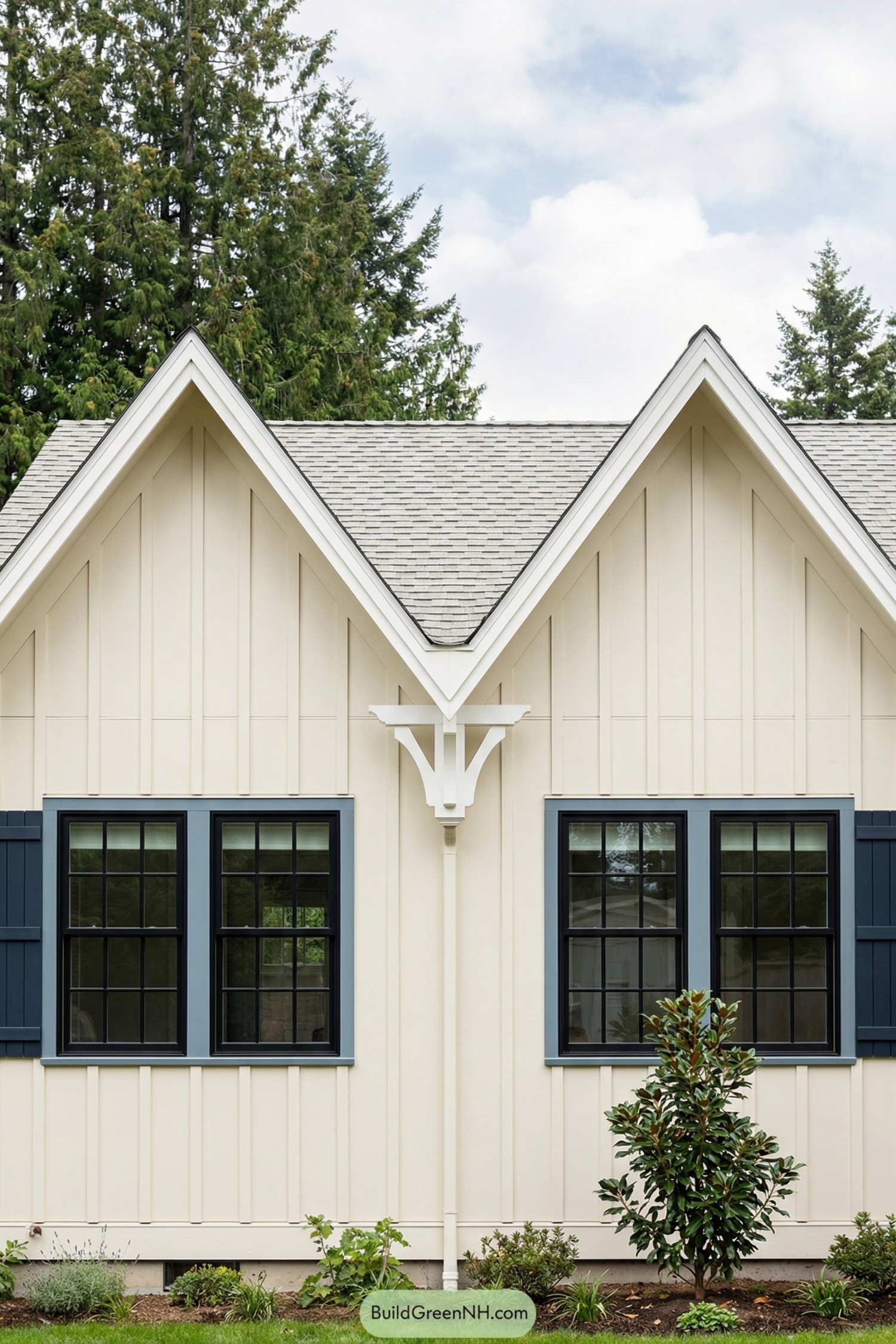 Cream vertical-siding cottage with twin peaked gables, navy-framed windows, and simple front landscaping