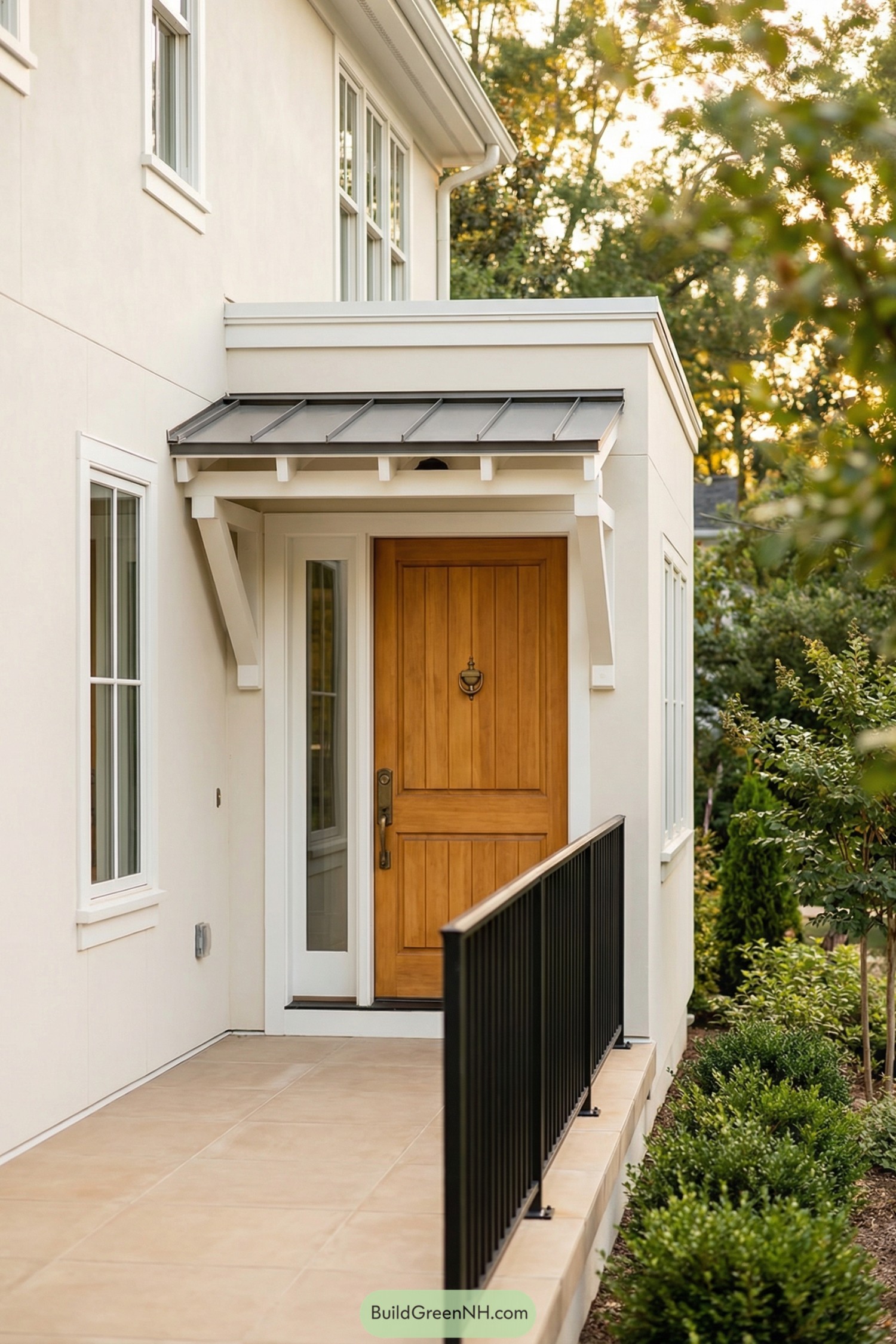 Warm wood front door under small metal awning with simple black railing and light stucco walls