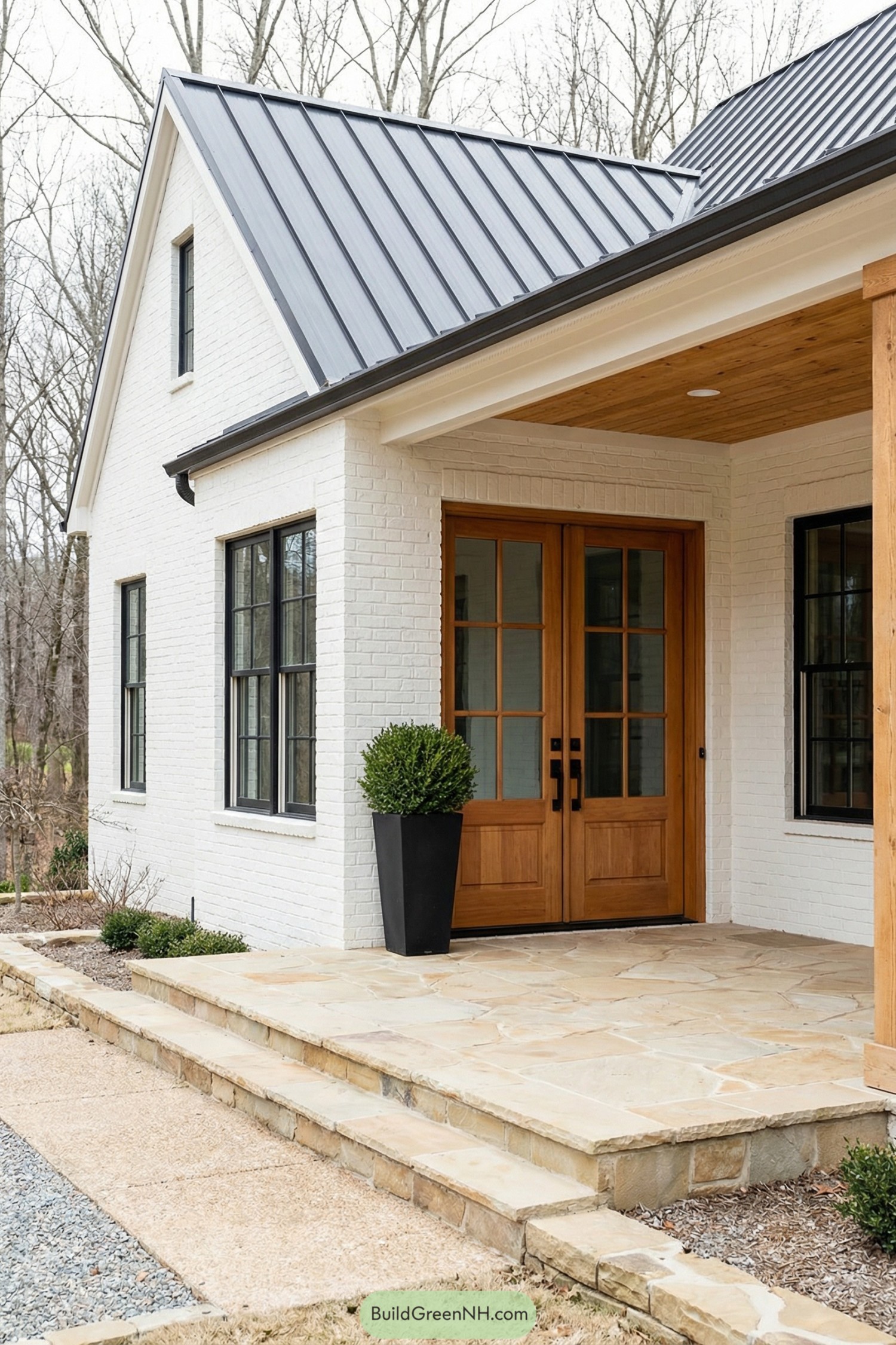 Modern farmhouse entry with double wooden doors, white painted brick, black-framed windows, and a stone porch with planter