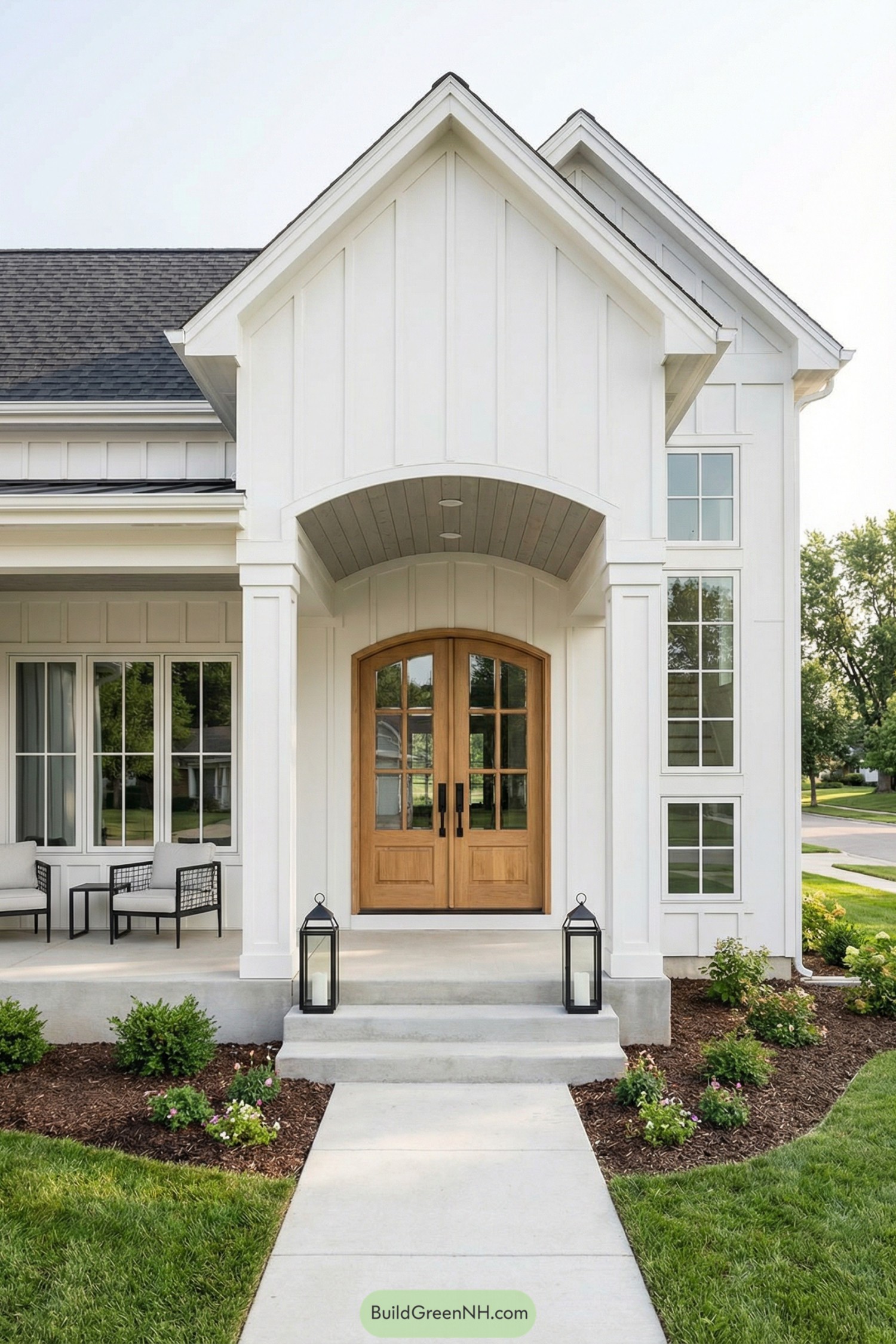 White farmhouse-style front entry with arched double wood doors, tall gable, side porch seating, and simple landscaping