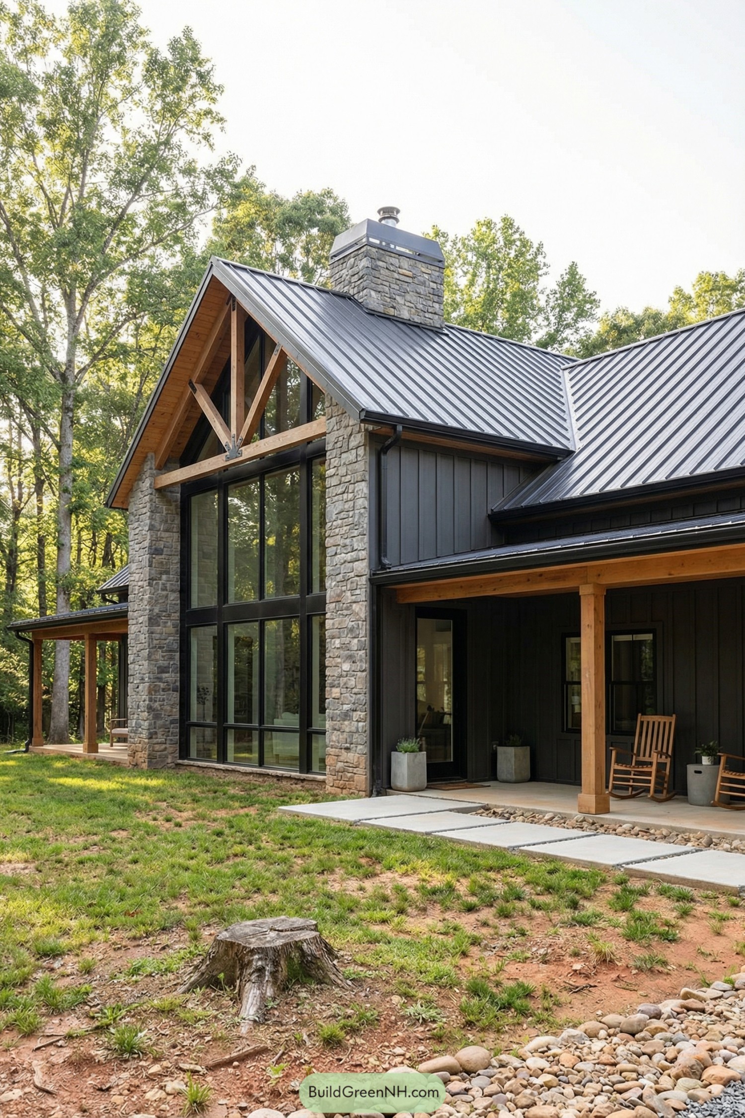 Modern barndominium with dark siding, stone chimney, and large glass front overlooking a wooded yard