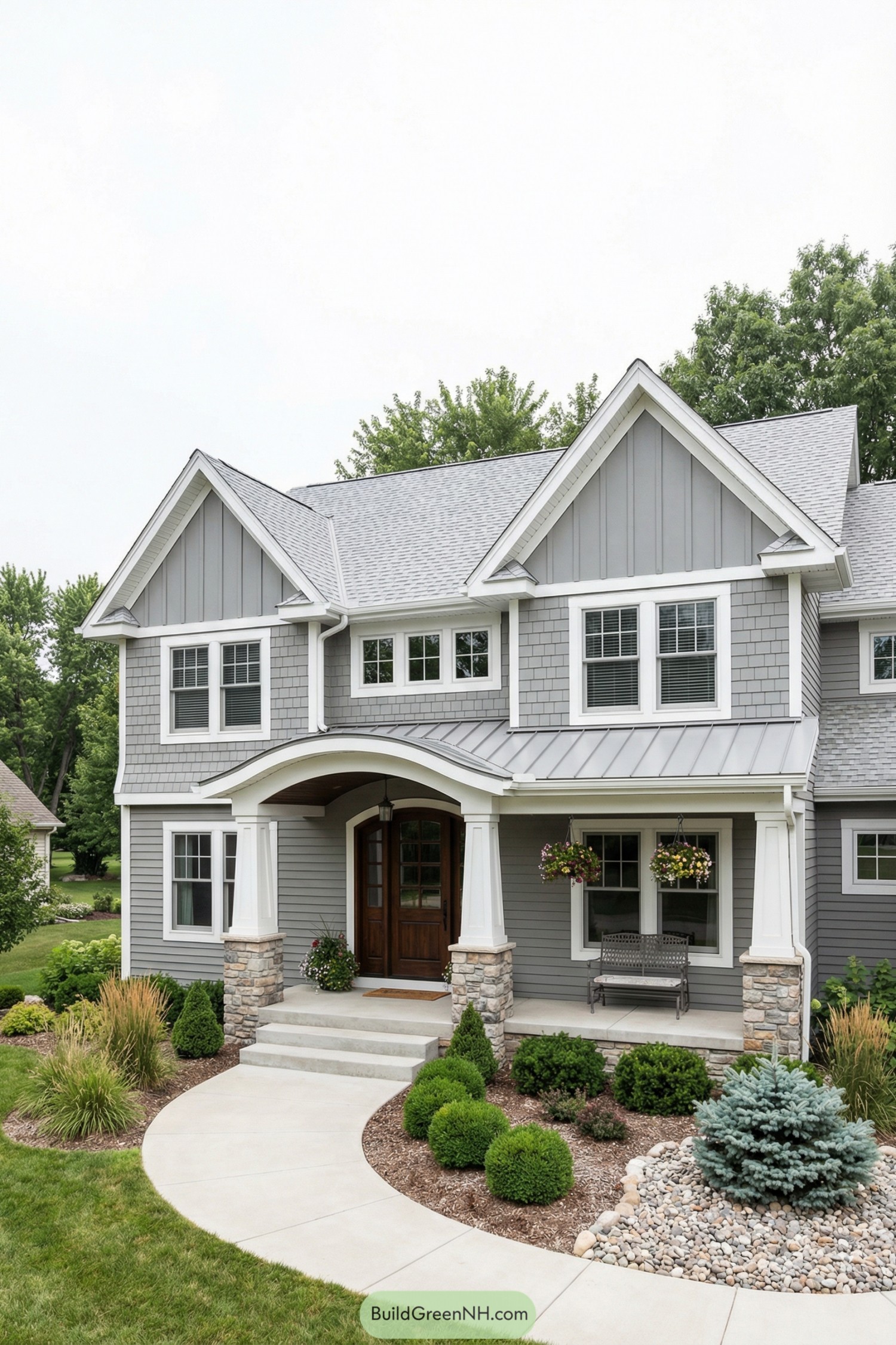 Two-story grey house with white trim, gabled roof, and a curved walkway through manicured landscaping